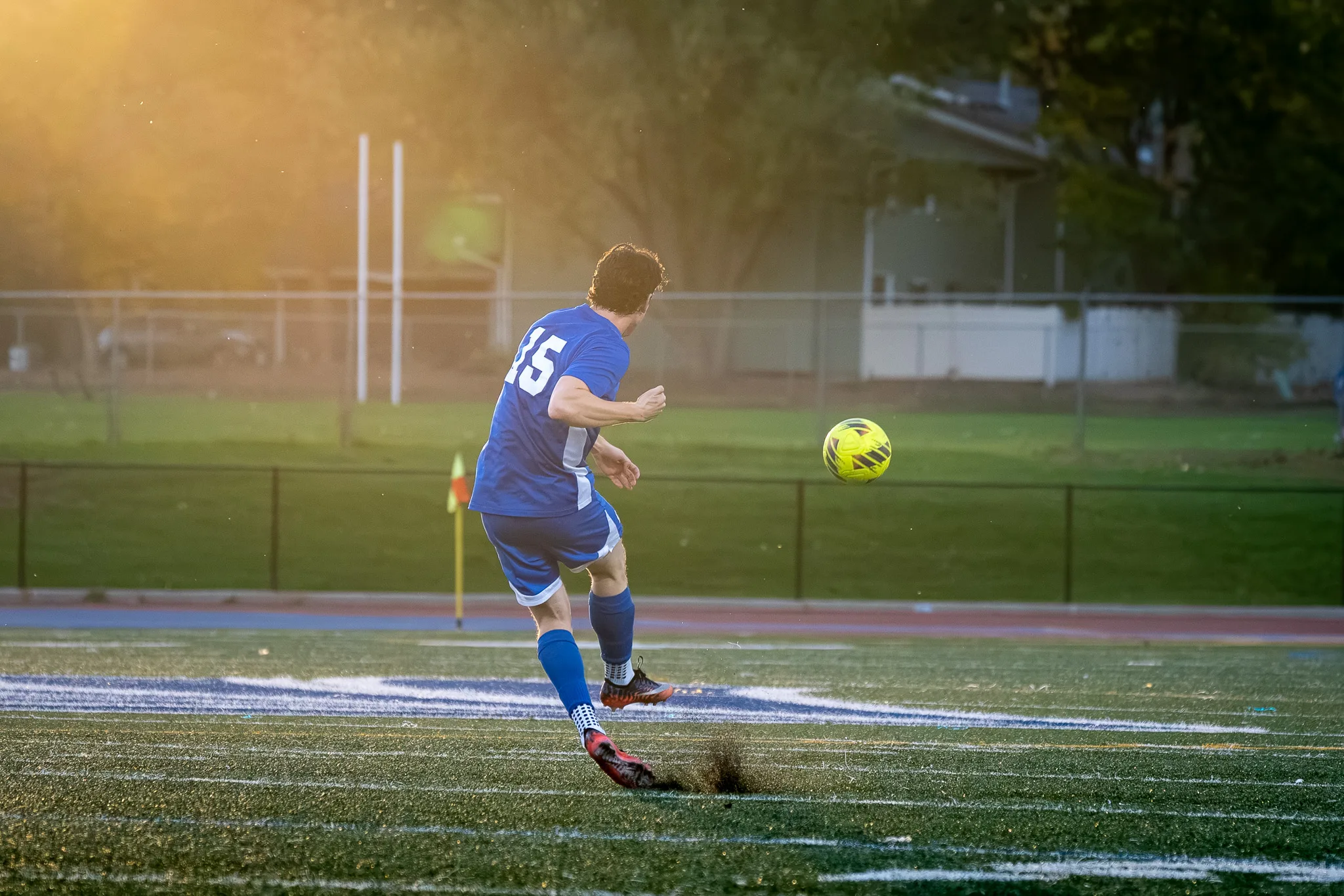 Turf kicks up as a Centaurus player strikes the ball, the low sun glowing through the trees behind him