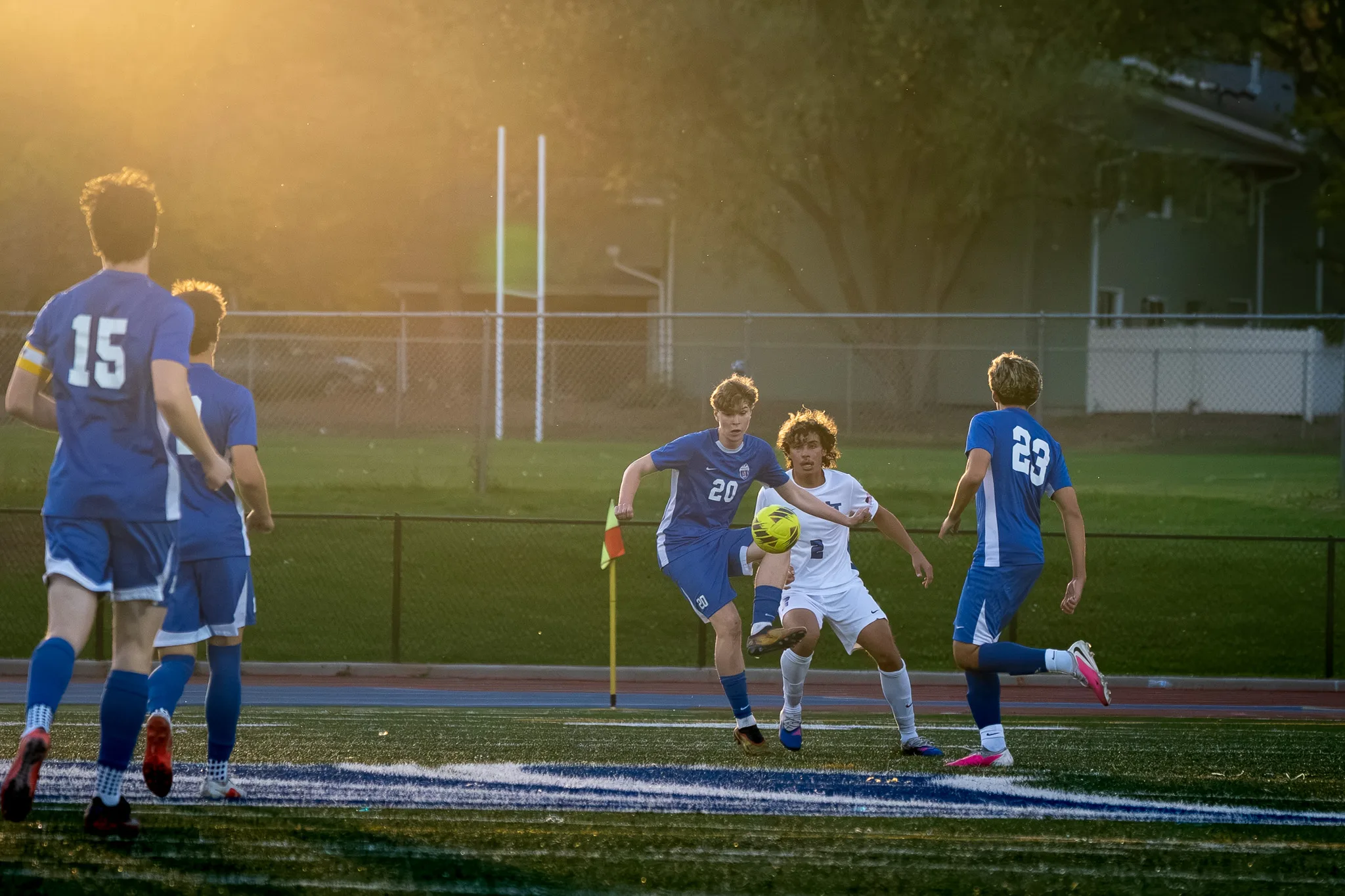 In low golden light, Centaurus number 20 kicks the ball with a Longmont player beside him, Centaurus numbers 15 and 23 nearby