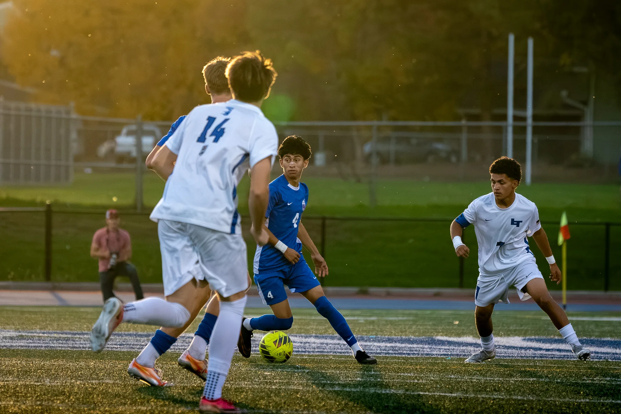 In the warm evening light, Centaurus number 4 dribbles between Longmont number 14 and another Longmont player
