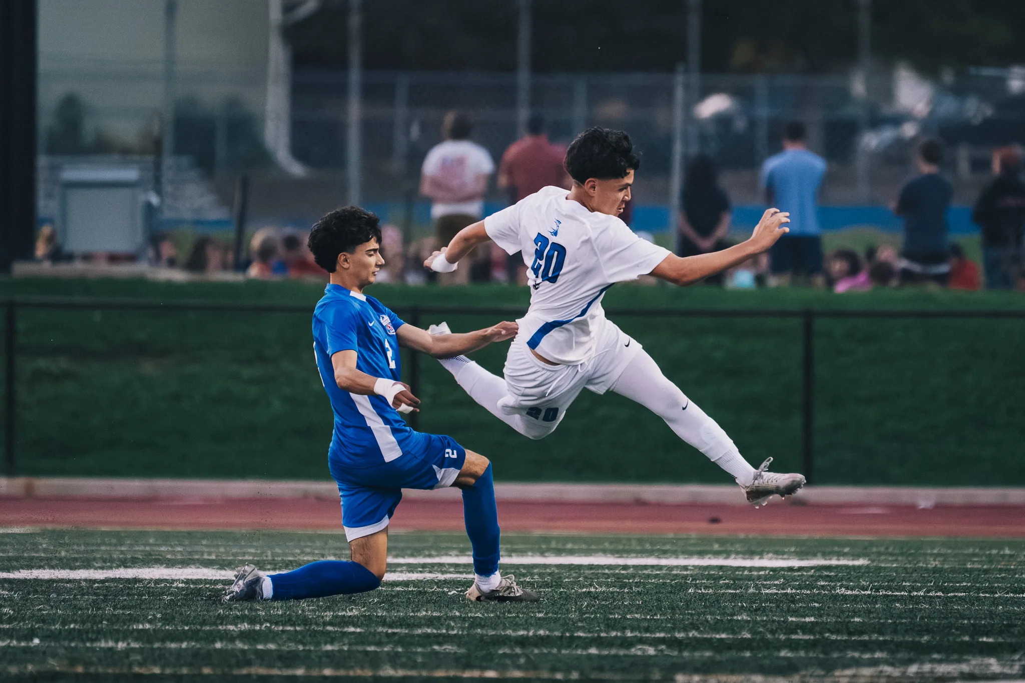 A Longmont player jumps past Centaurus number 2, who is down on one knee, with spectators on the hill behind