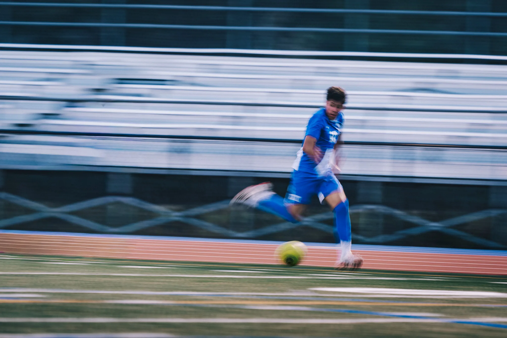 Along the sideline, a Centaurus player runs with the ball in a motion blur, the bleachers streaking behind him