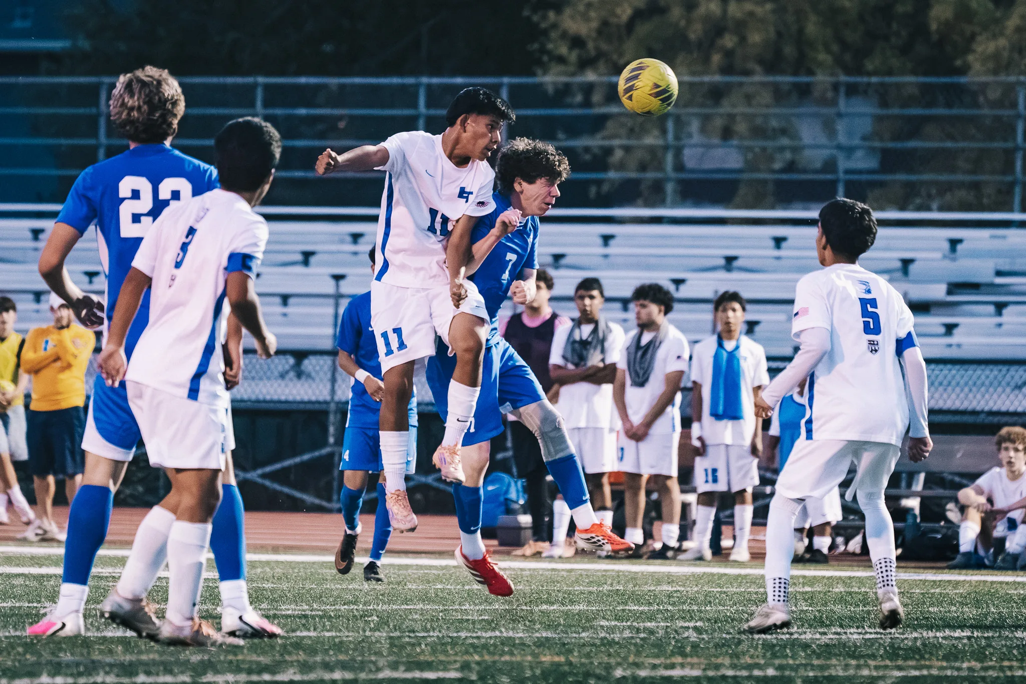 Longmont number 11 and Centaurus number 7 rise together for a header, substitutes lined up on the sideline behind them
