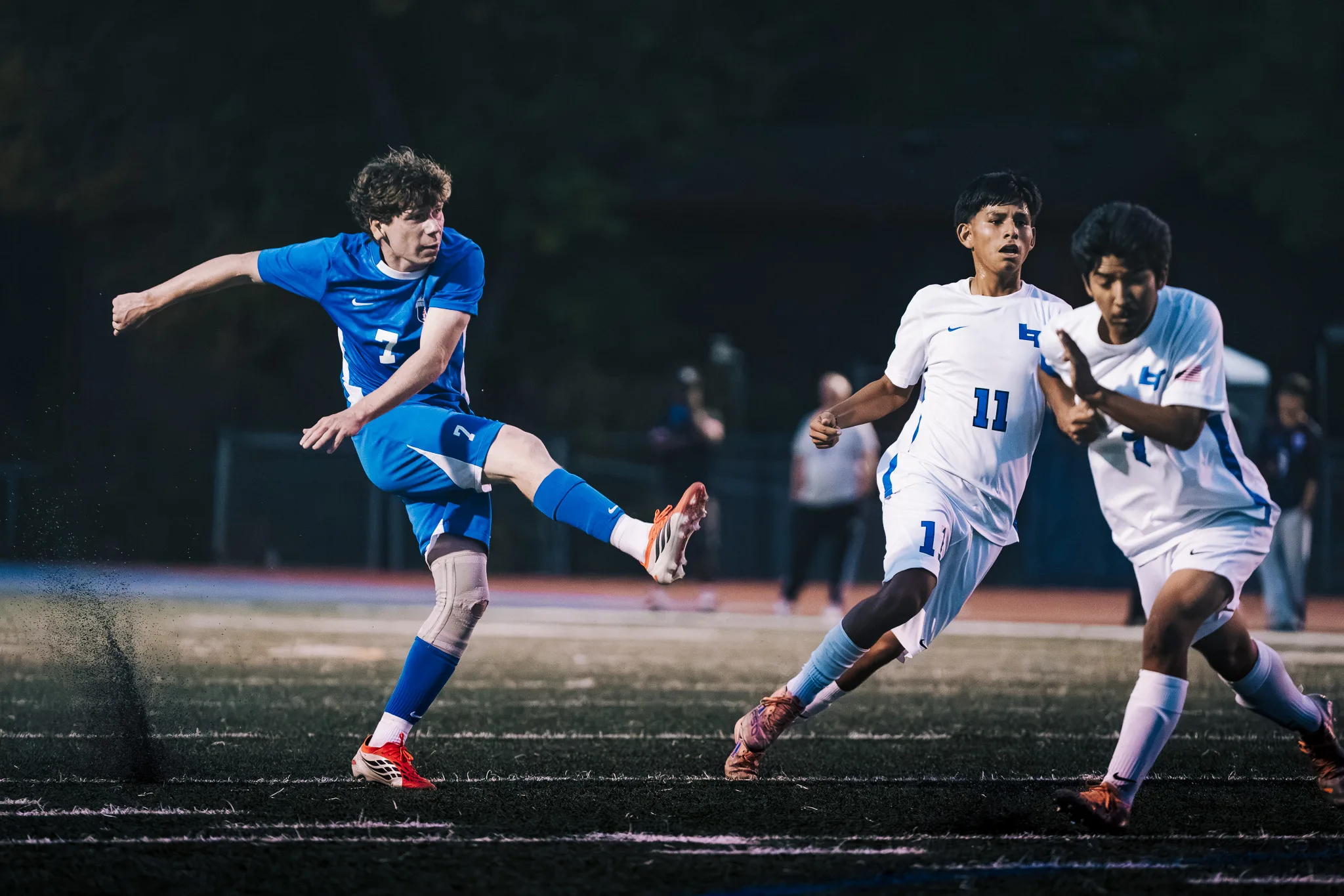 Turf sprays up as Centaurus number 7 swings his leg through a kick, with Longmont number 11 and another Longmont player running in