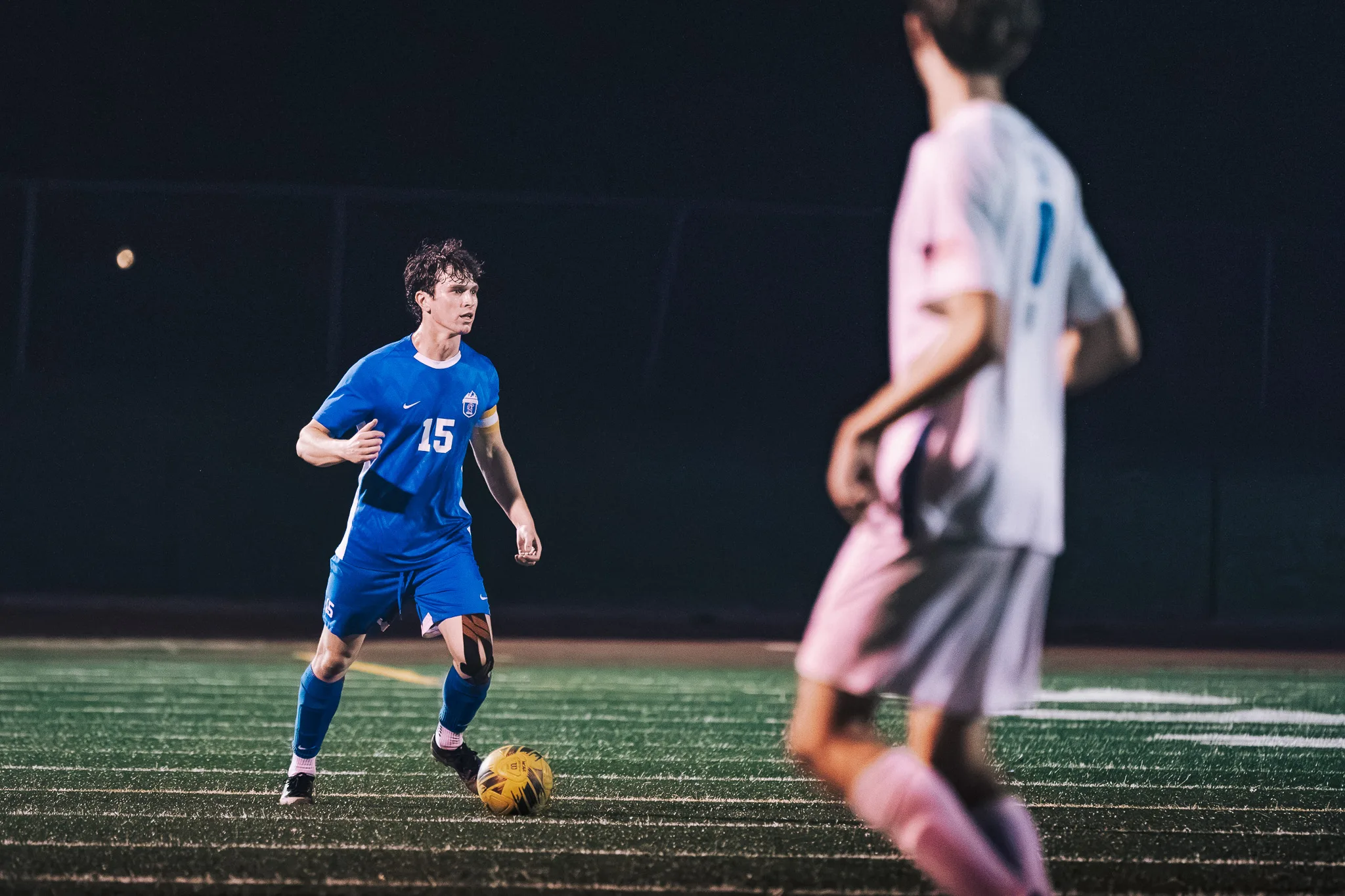 With the ball at his feet, Centaurus number 15 looks up as a blurred Longmont player moves through the foreground