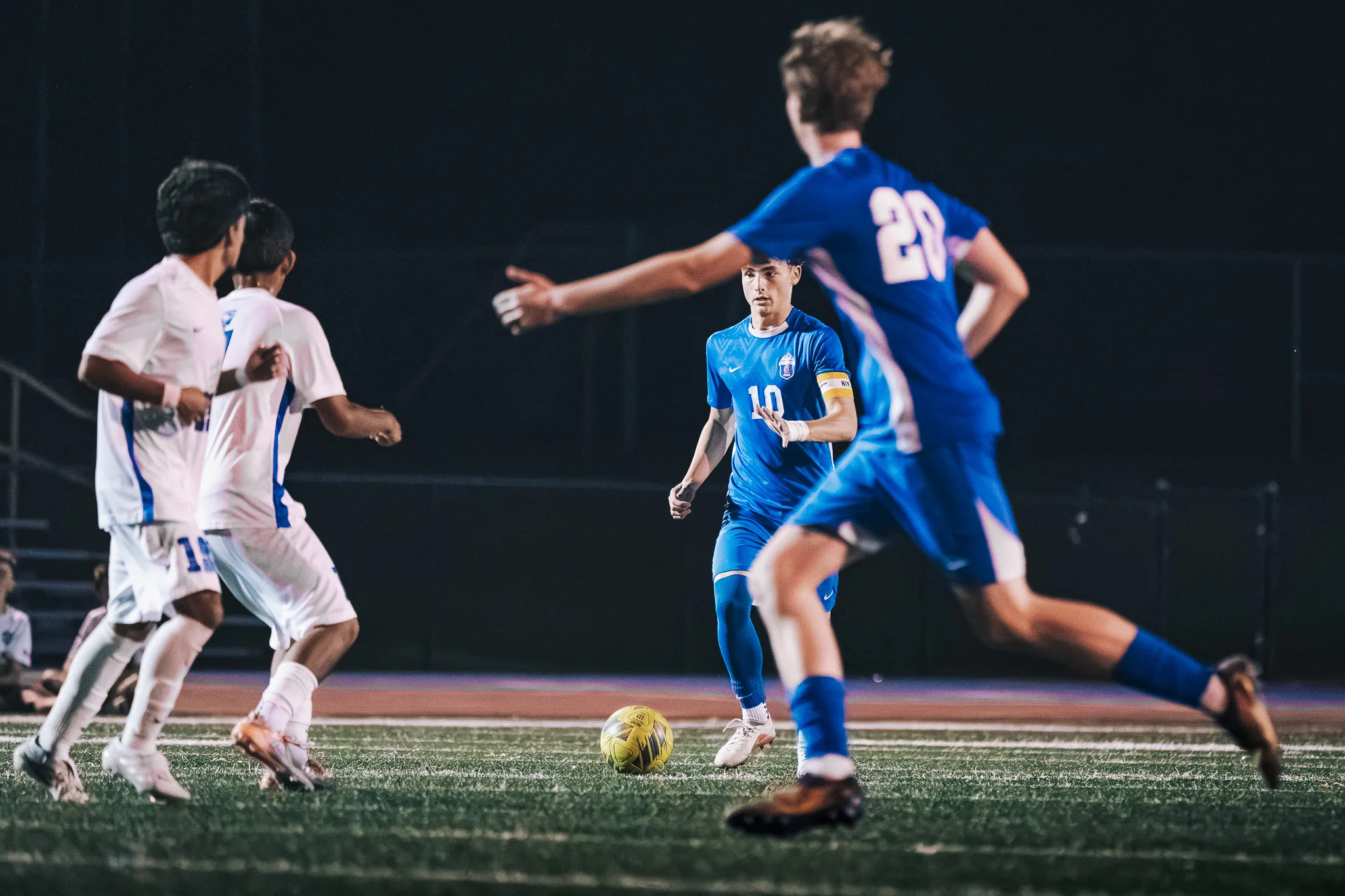 Two Longmont players run in from the left as Centaurus number 10 stands near the ball and number 20 strides across the foreground