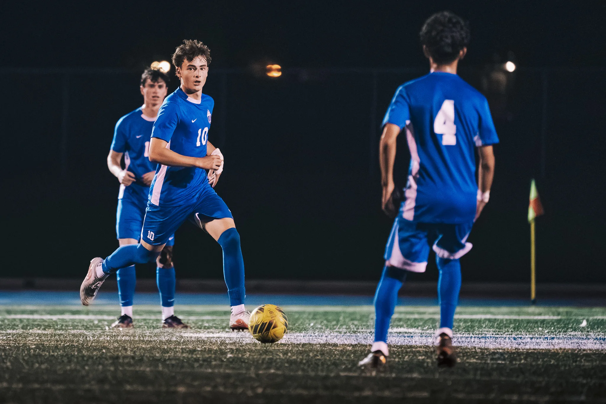 Centaurus number 4 faces teammate number 10, who looks up with the ball at his feet as another teammate follows