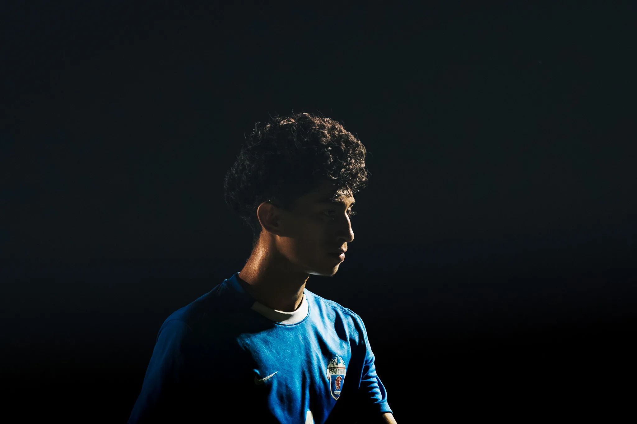 Lit by a single shaft of light, a Centaurus player looks off to the side against a black backdrop
