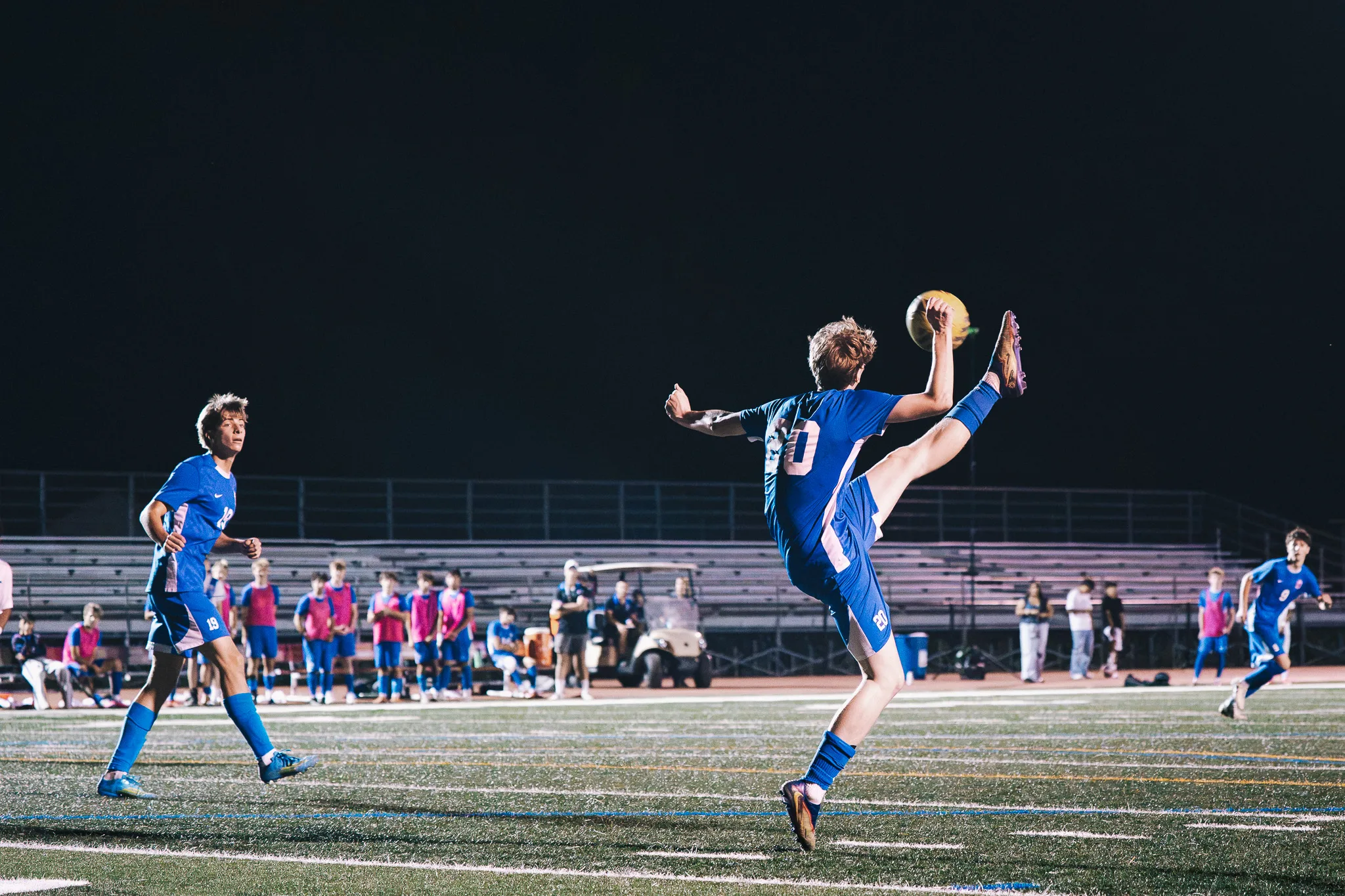 Leg raised high, Centaurus number 20 stretches for the ball with the Centaurus bench in pink bibs behind him