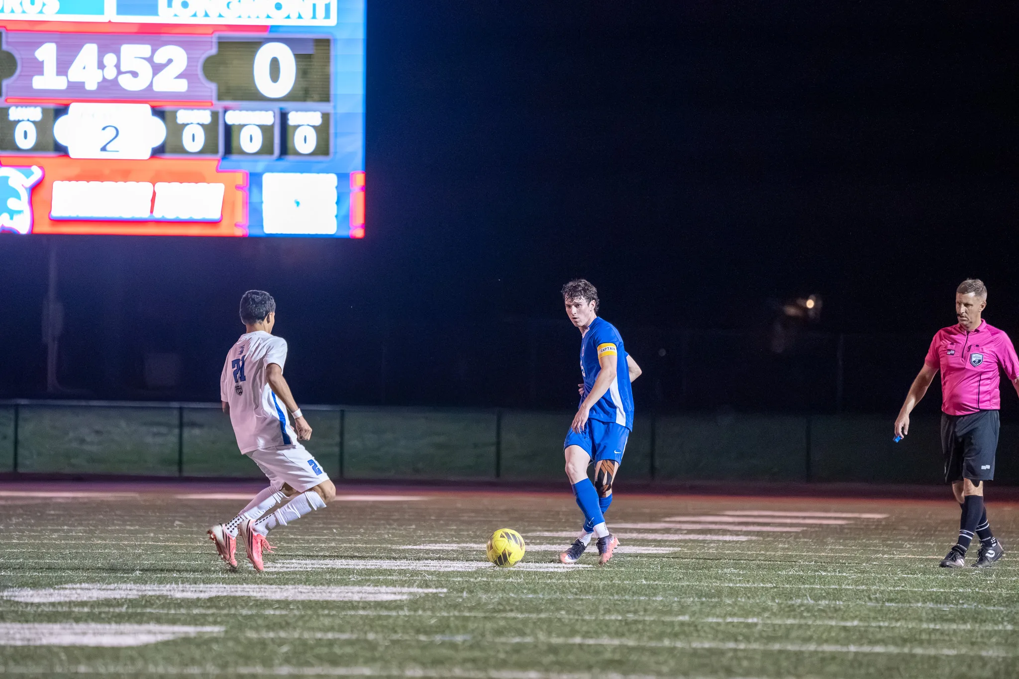 With the ball between them, a Longmont player and a Centaurus player face off beneath the glowing scoreboard