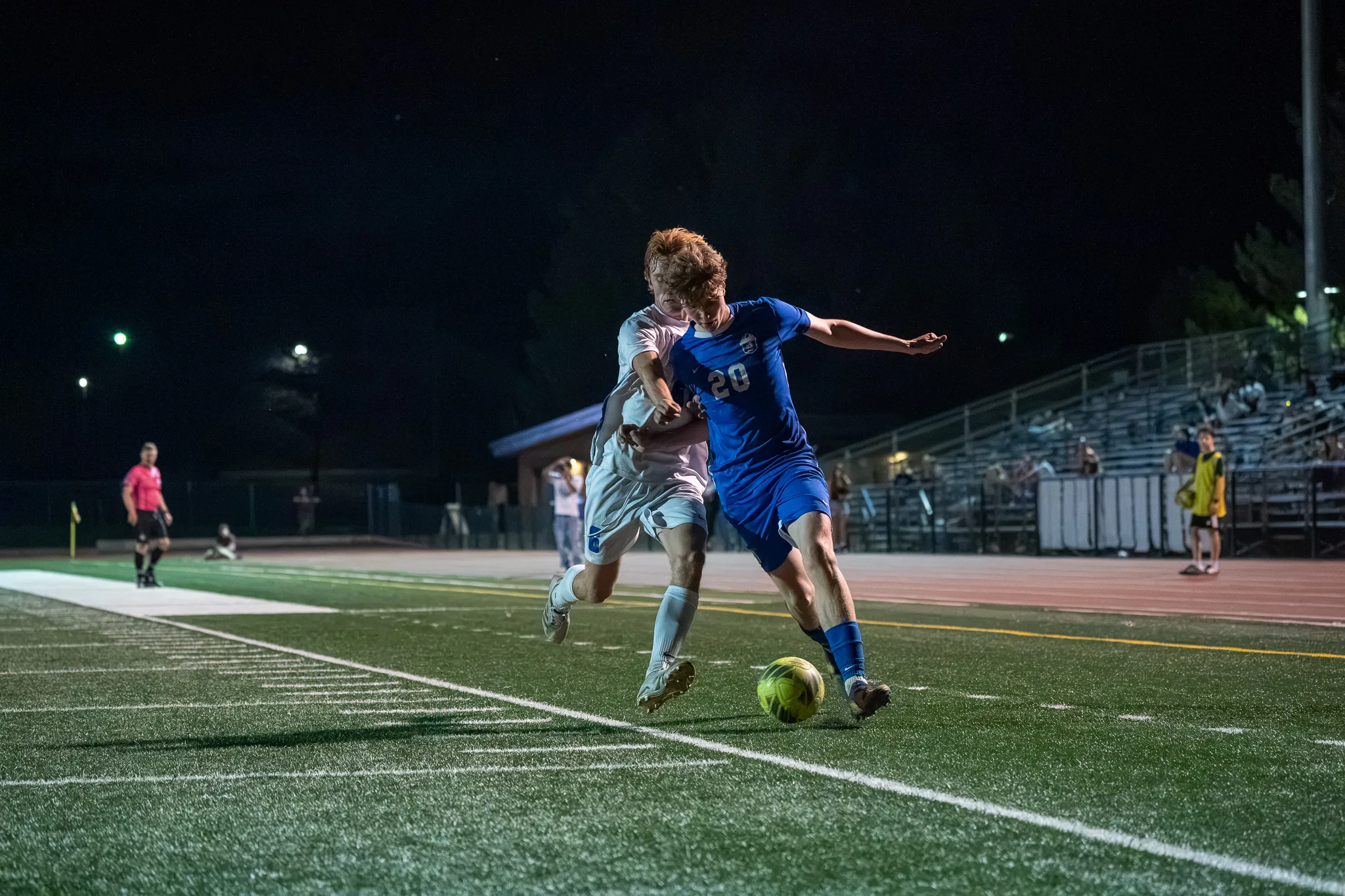 Along the sideline, Centaurus number 20 and a Longmont player battle shoulder to shoulder for the ball, bleachers behind