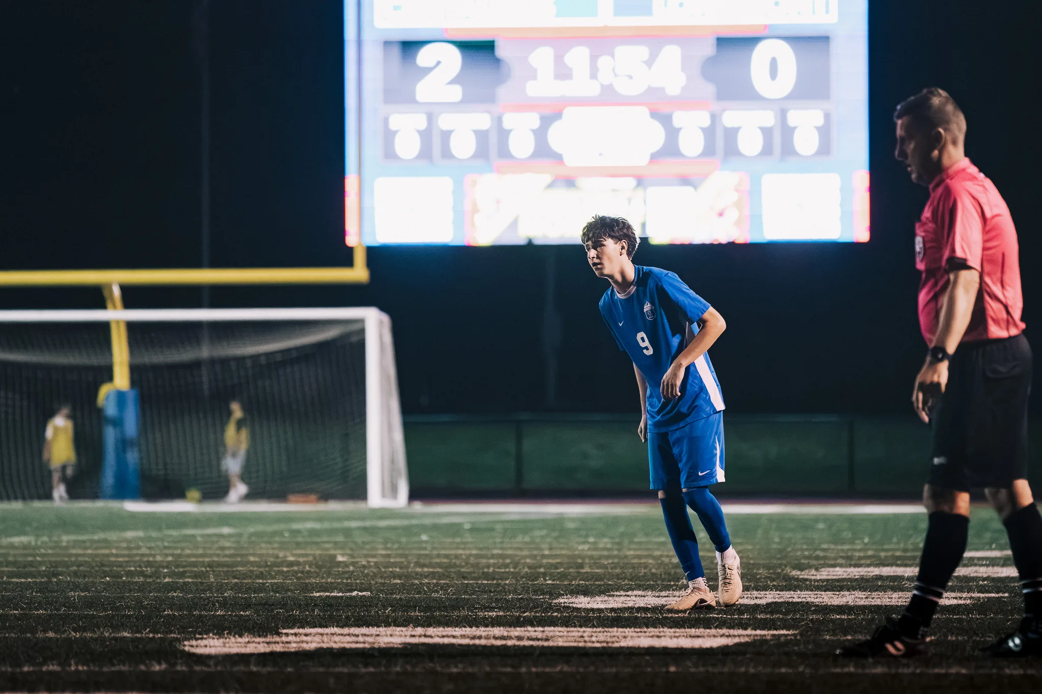 Crouched with his weight forward, Centaurus number 9 waits as the scoreboard glows in the dark behind him