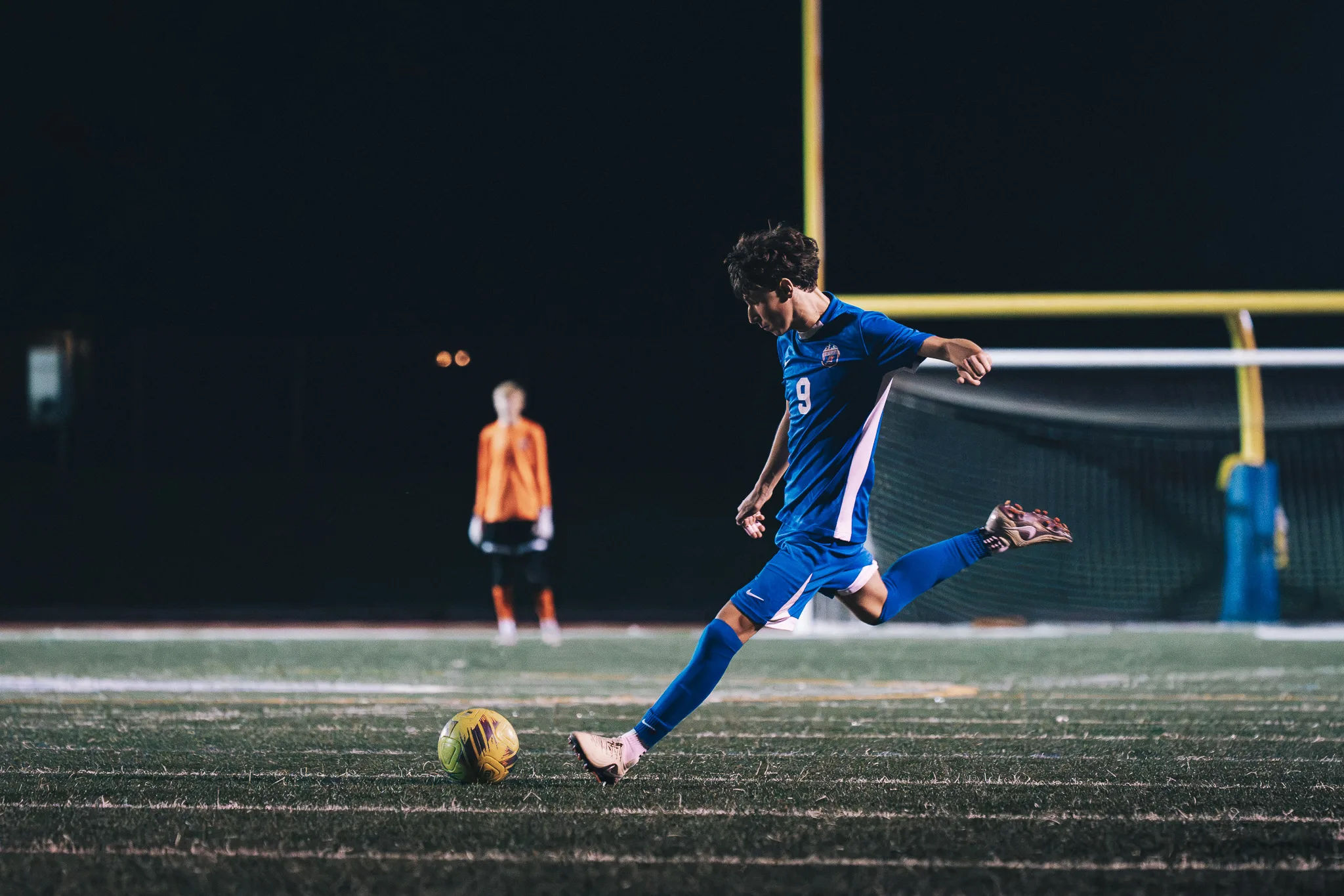 Eyes on the ball, Centaurus number 9 draws his leg back to strike it, the Centaurus goalkeeper in orange standing in the distance