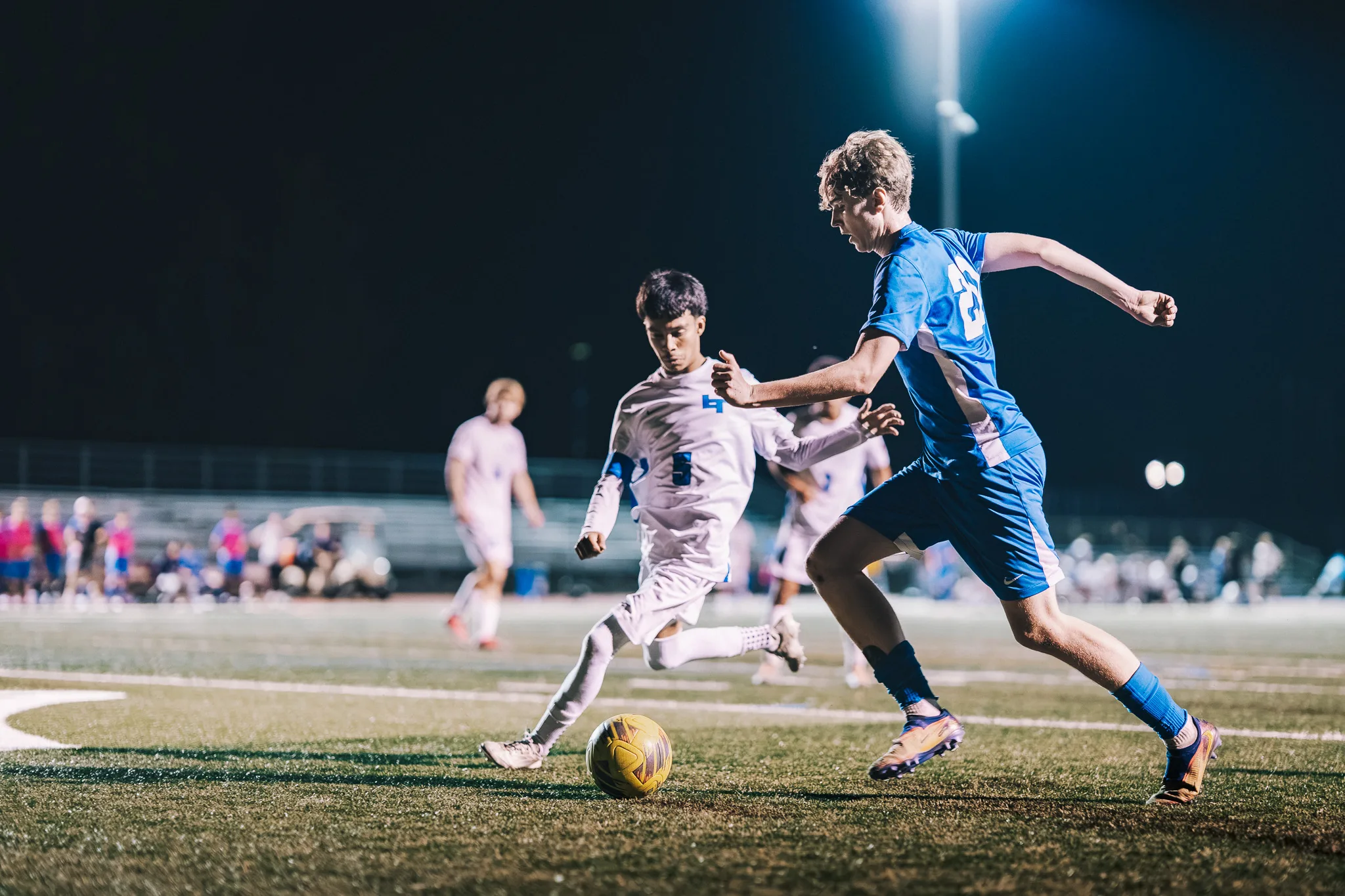 From opposite sides, Longmont number 5 and a Centaurus player close in on the ball, a stadium light glowing above