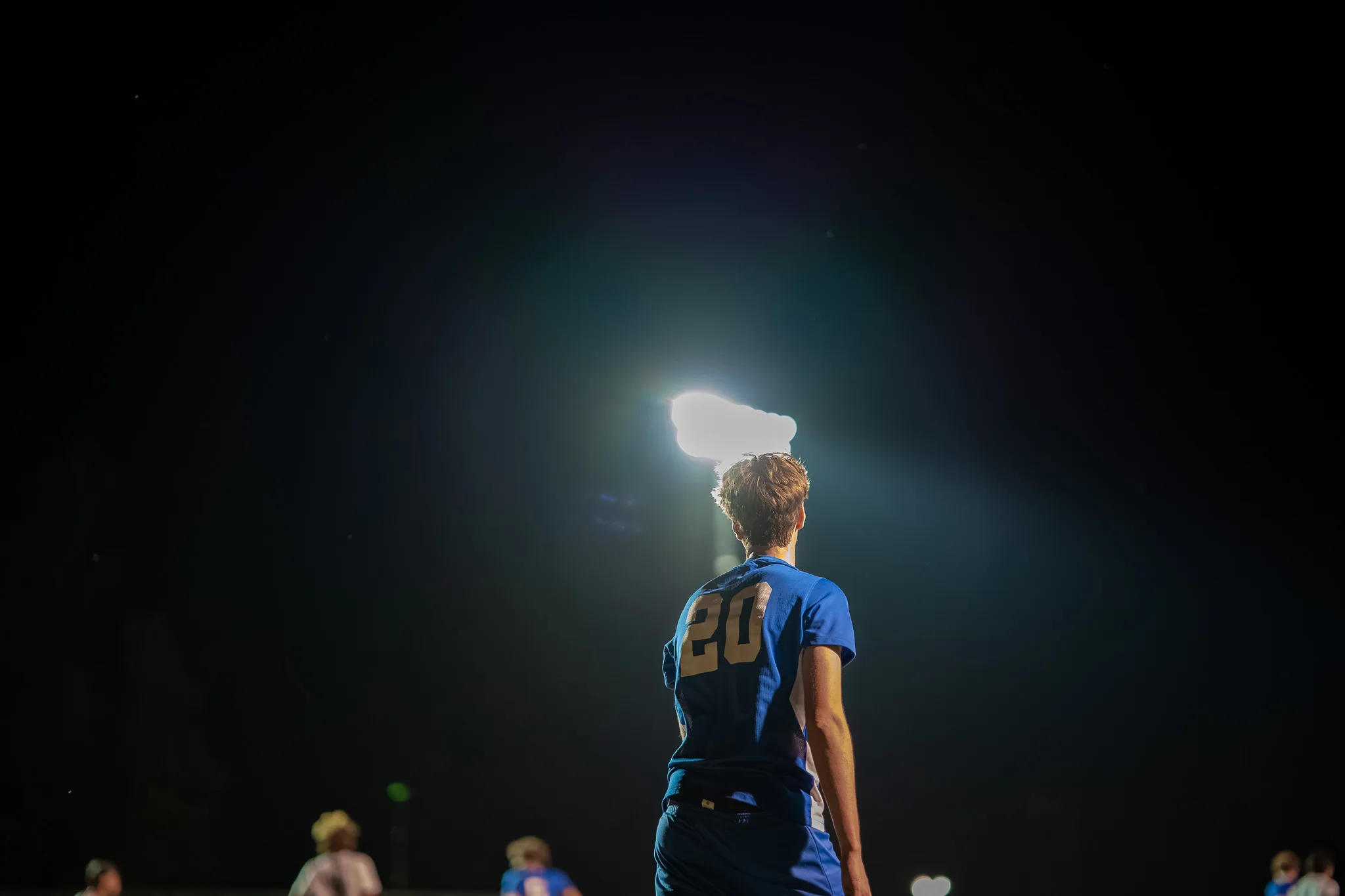 Seen from behind, Centaurus number 20 stands in the dark with a bright stadium light glowing above his head