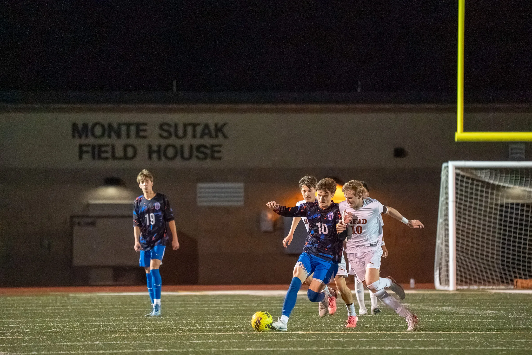 Centaurus number 10 and Mead number 10 battle for the ball in front of the field house while Centaurus number 19 watches from the left