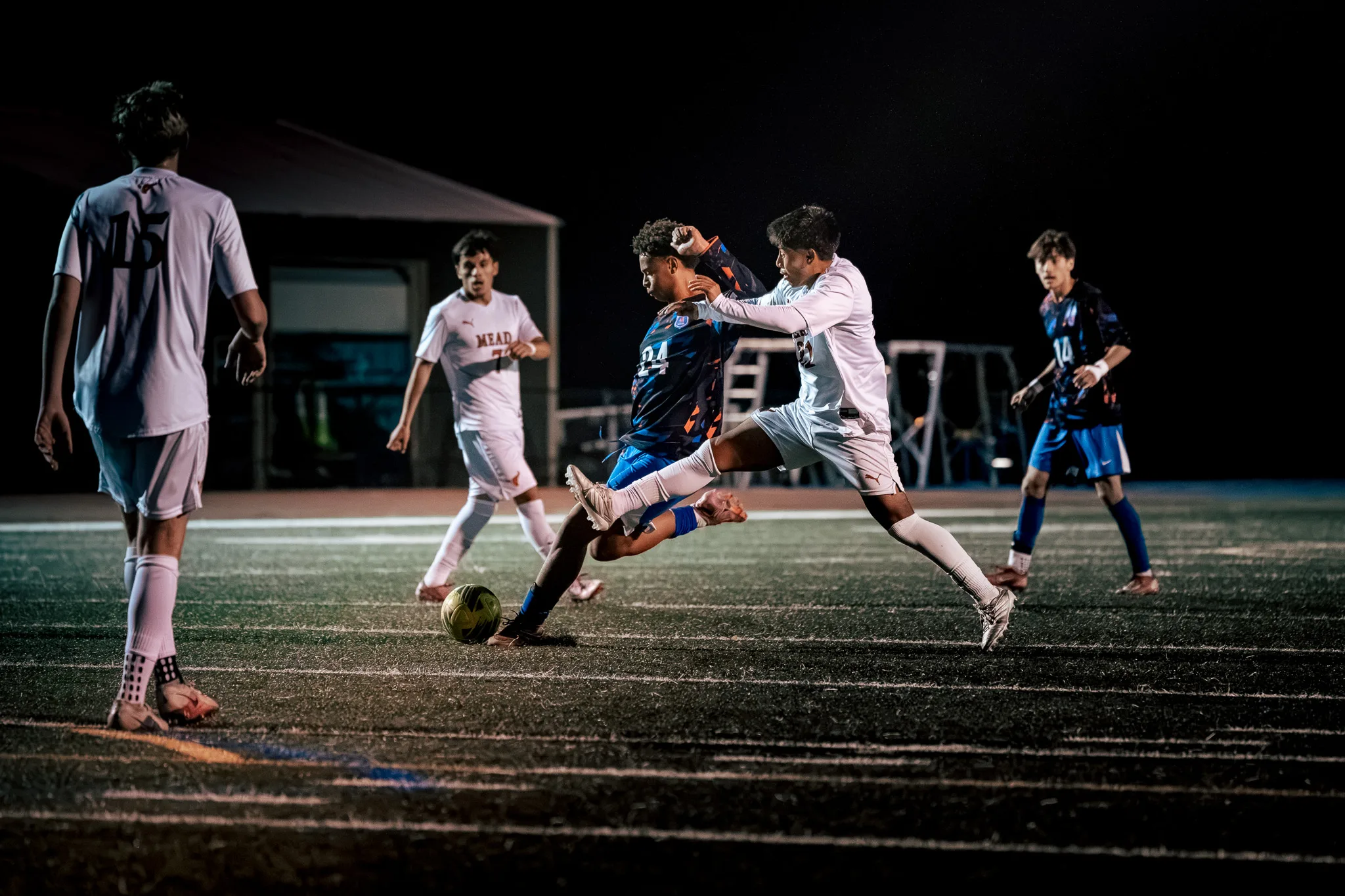 Centaurus number 24 and a Mead player scramble for the ball with their legs tangled as Mead number 15 stands in the foreground, Mead number 7 looks on and a Centaurus teammate approaches from the right