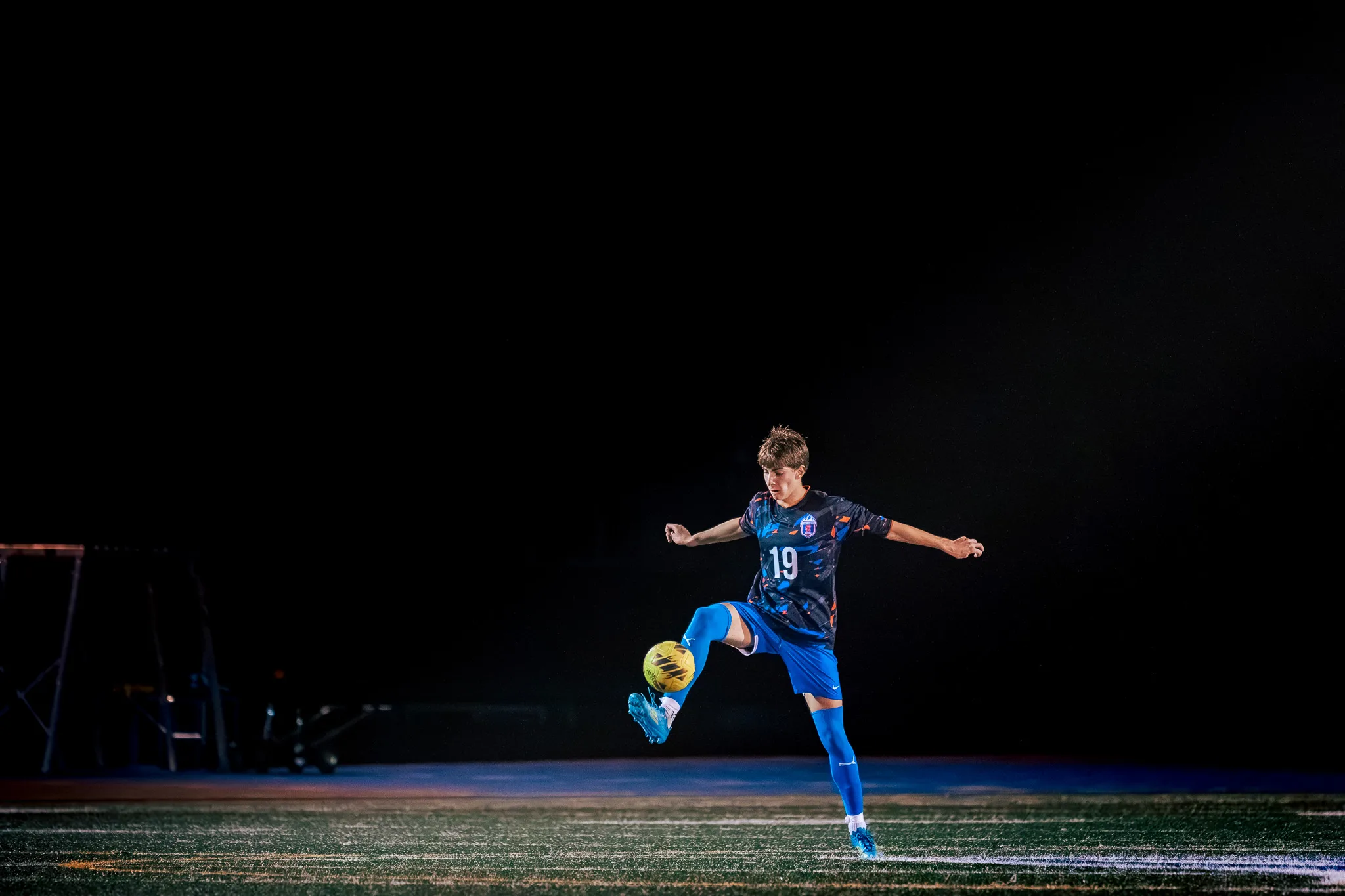 Centaurus number 19 lifts the ball with a raised leg, arms spread for balance, alone in a pool of stadium light against a black sky