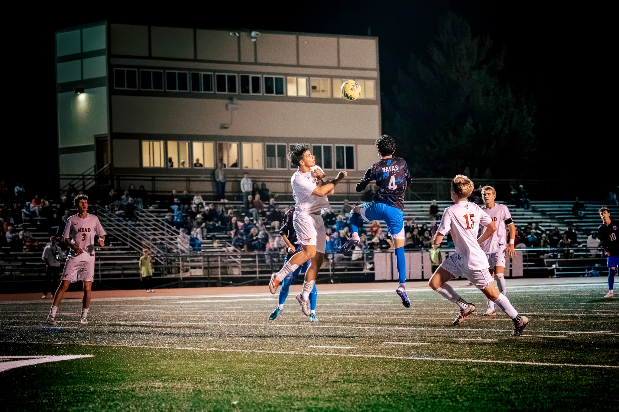 Centaurus number 4 and a Mead player leap together to head the ball in front of crowded bleachers, with Mead numbers 15 and 3 and Centaurus number 10 nearby