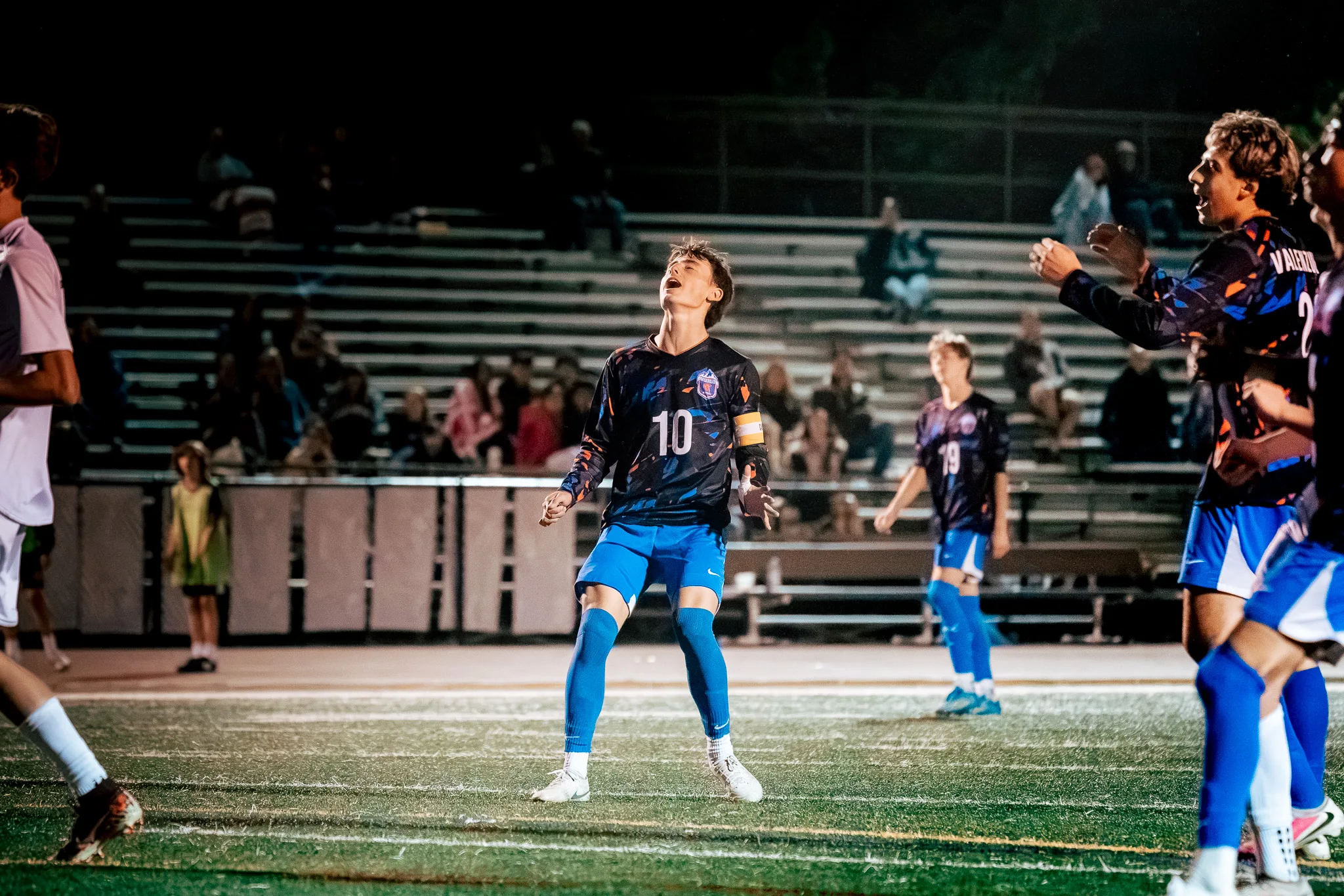 Head tipped back and arms spread, Centaurus number 10 in a captain's armband reacts to the play as Centaurus number 19 stands behind him and teammates at the right edge call out
