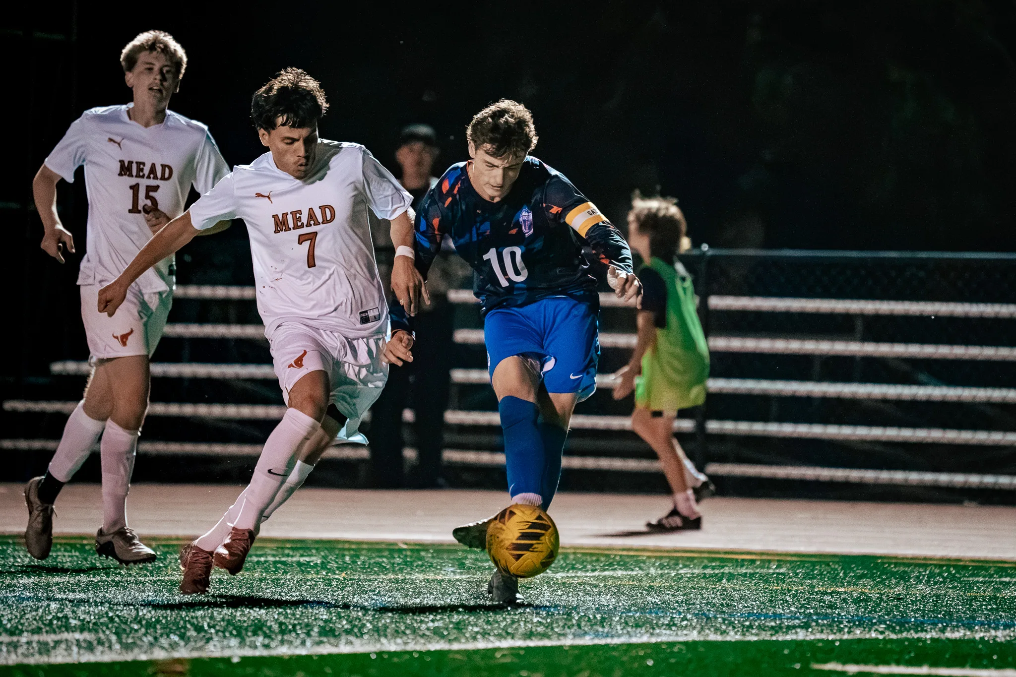 Centaurus number 10, wearing a captain's armband, takes the ball forward with Mead number 7 on his shoulder and Mead number 15 chasing behind