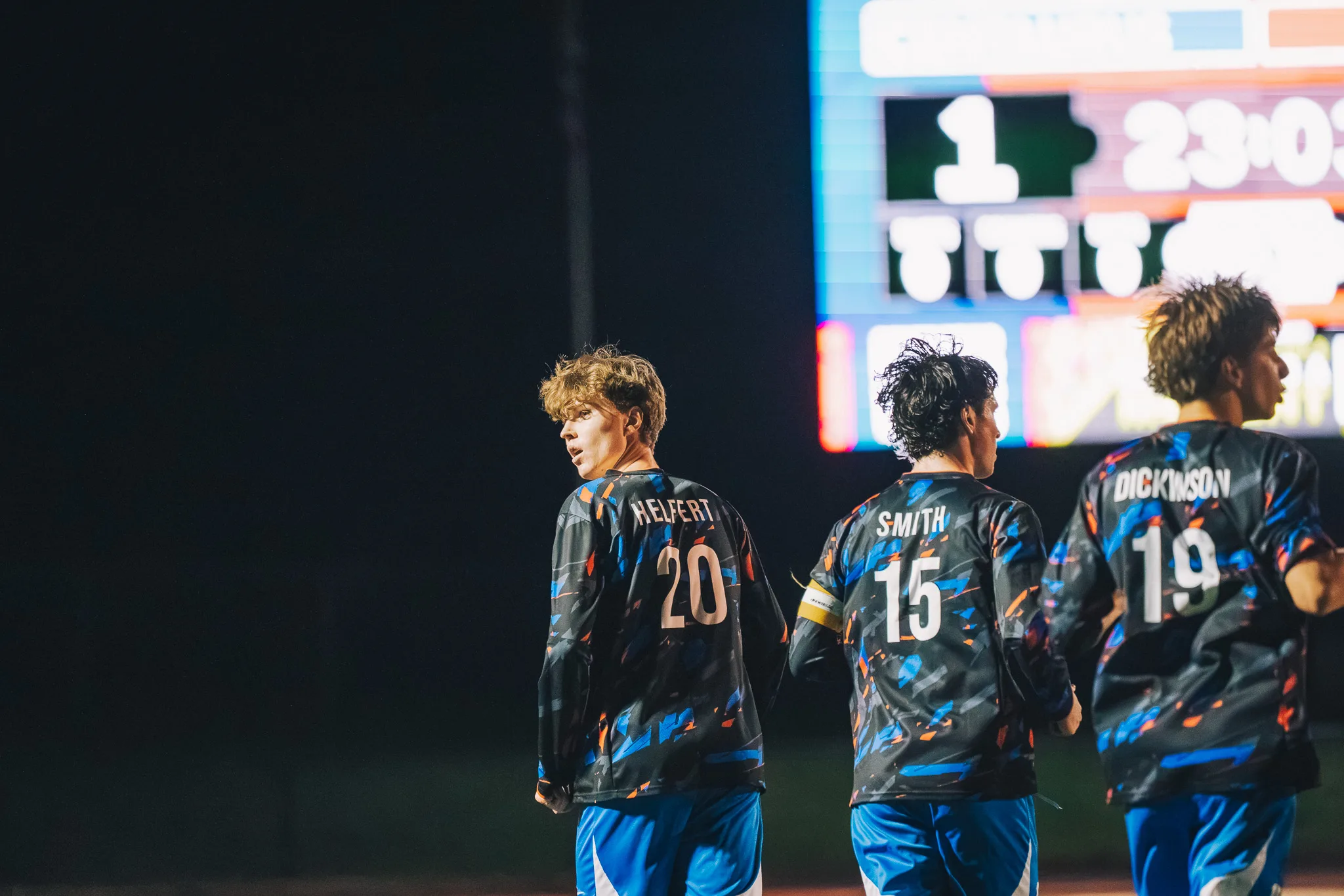 Seen from behind, Centaurus numbers 20, 15 and 19 jog along together, number 20 glancing back over his shoulder, the scoreboard glowing behind them