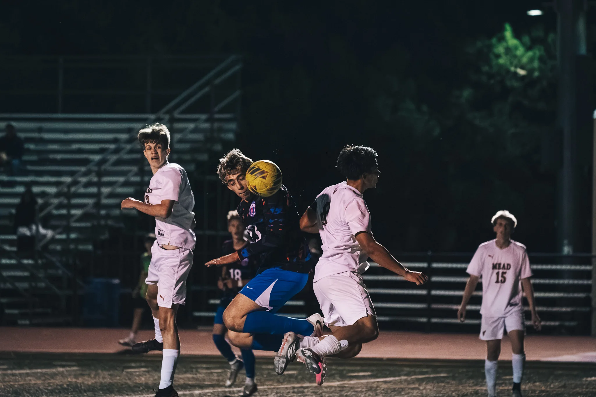 A Centaurus player heads the ball as a Mead player leaps in beside him, with a second Mead player standing at the left, Mead number 15 back at the right and Centaurus number 18 waiting behind