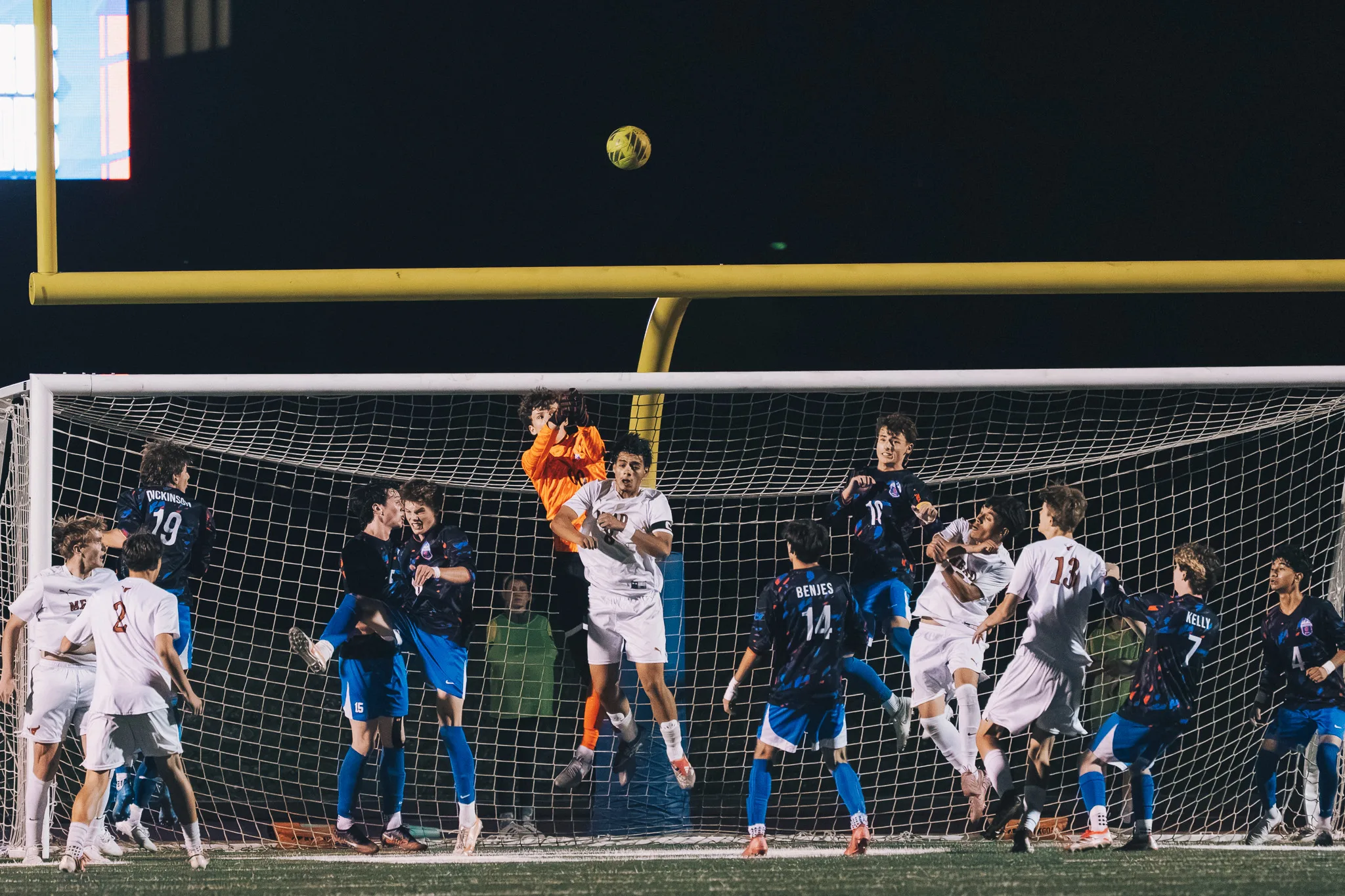 Players from both teams crowd the Centaurus goal as the goalkeeper in orange leaps with his arms up beside a Mead player, Centaurus numbers 19 and 14 and Mead numbers 2 and 13 among them, the ball high above the crossbar