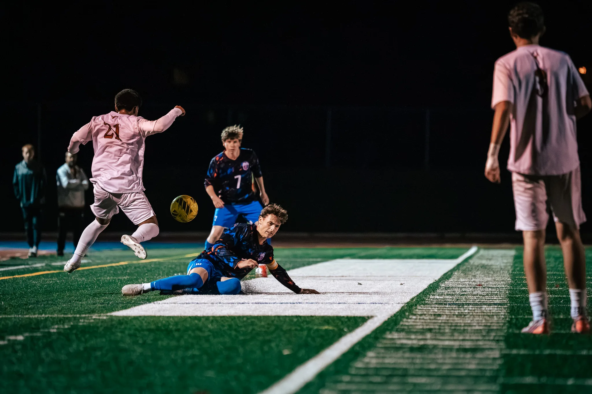 Mead number 21 swings his leg at the ball as a Centaurus player slides along the turf in front of him and Centaurus number 7 watches from behind