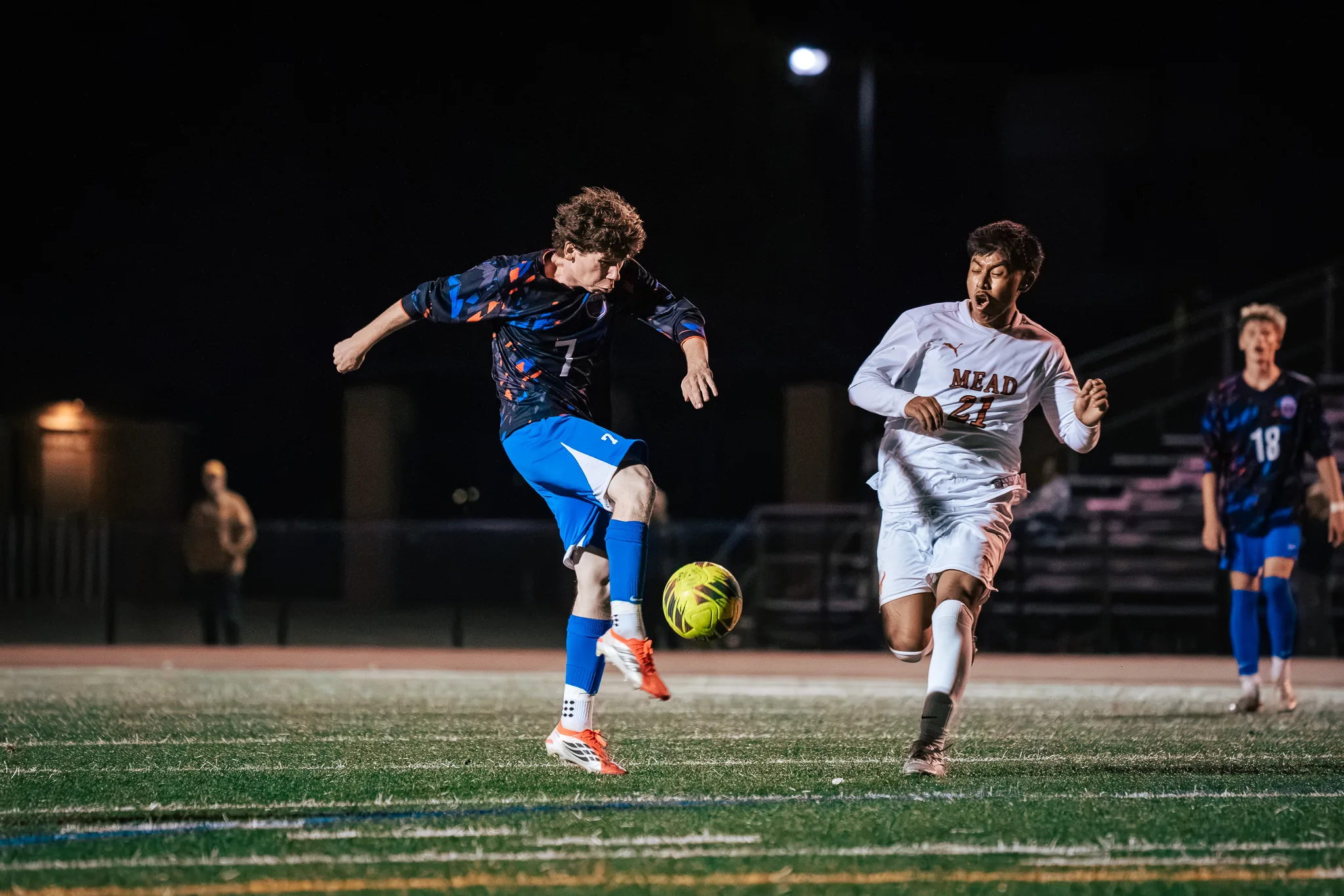 Centaurus number 7 swings his foot through the ball as Mead number 21 sprints alongside with his mouth open and Centaurus number 18 looks on from behind