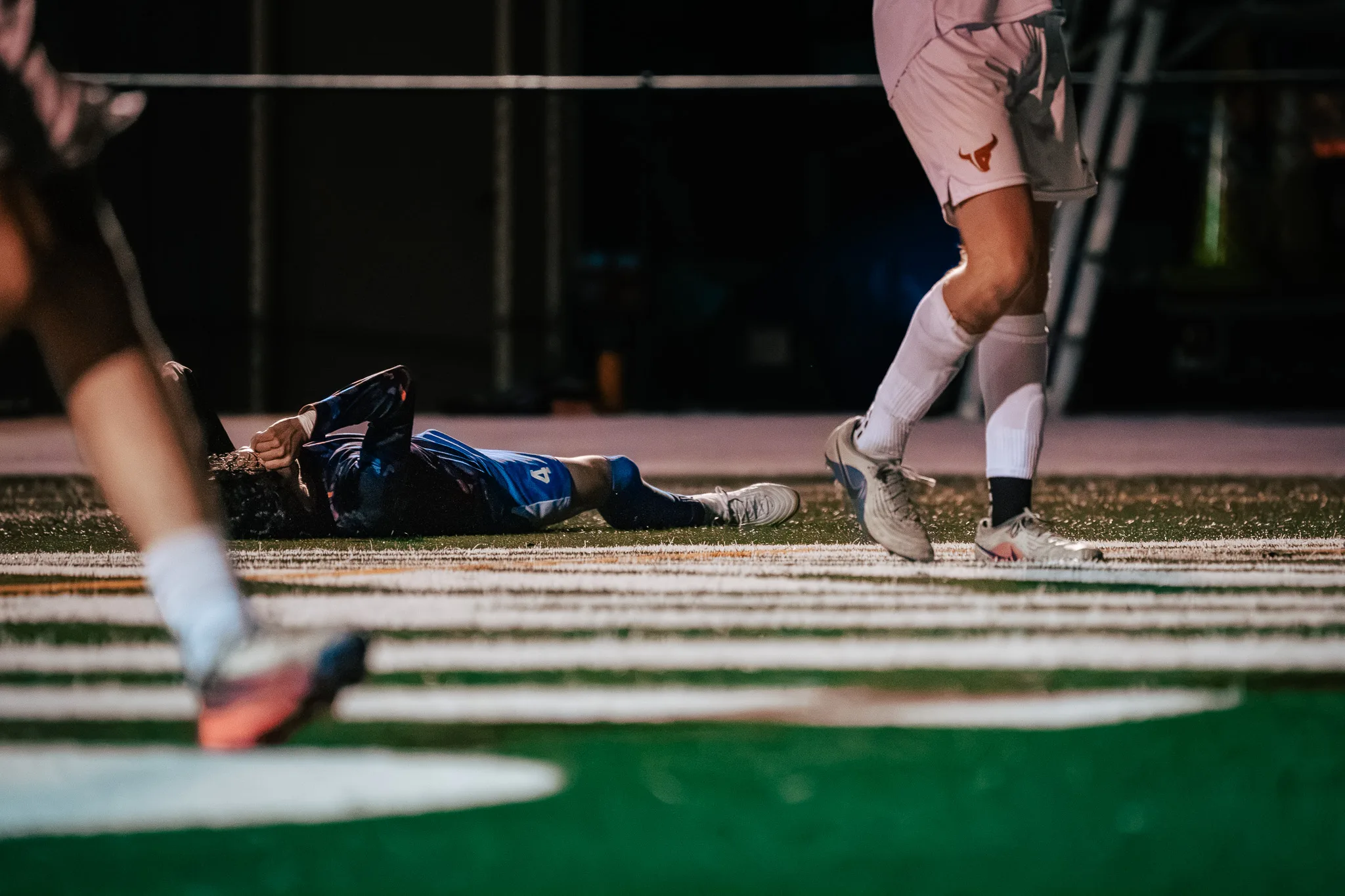 Low to the turf, a Centaurus player lies on his back with a hand at his face while Mead players' legs step past in the foreground