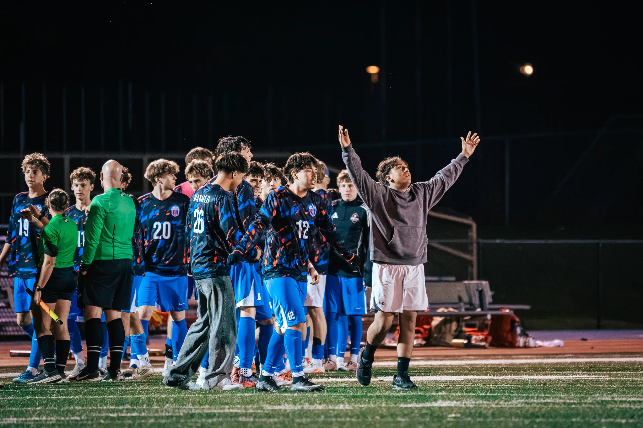 Centaurus players, including numbers 19, 20 and 12, gather along the sideline with two referees in green while a young man in a gray hoodie raises both arms and looks up