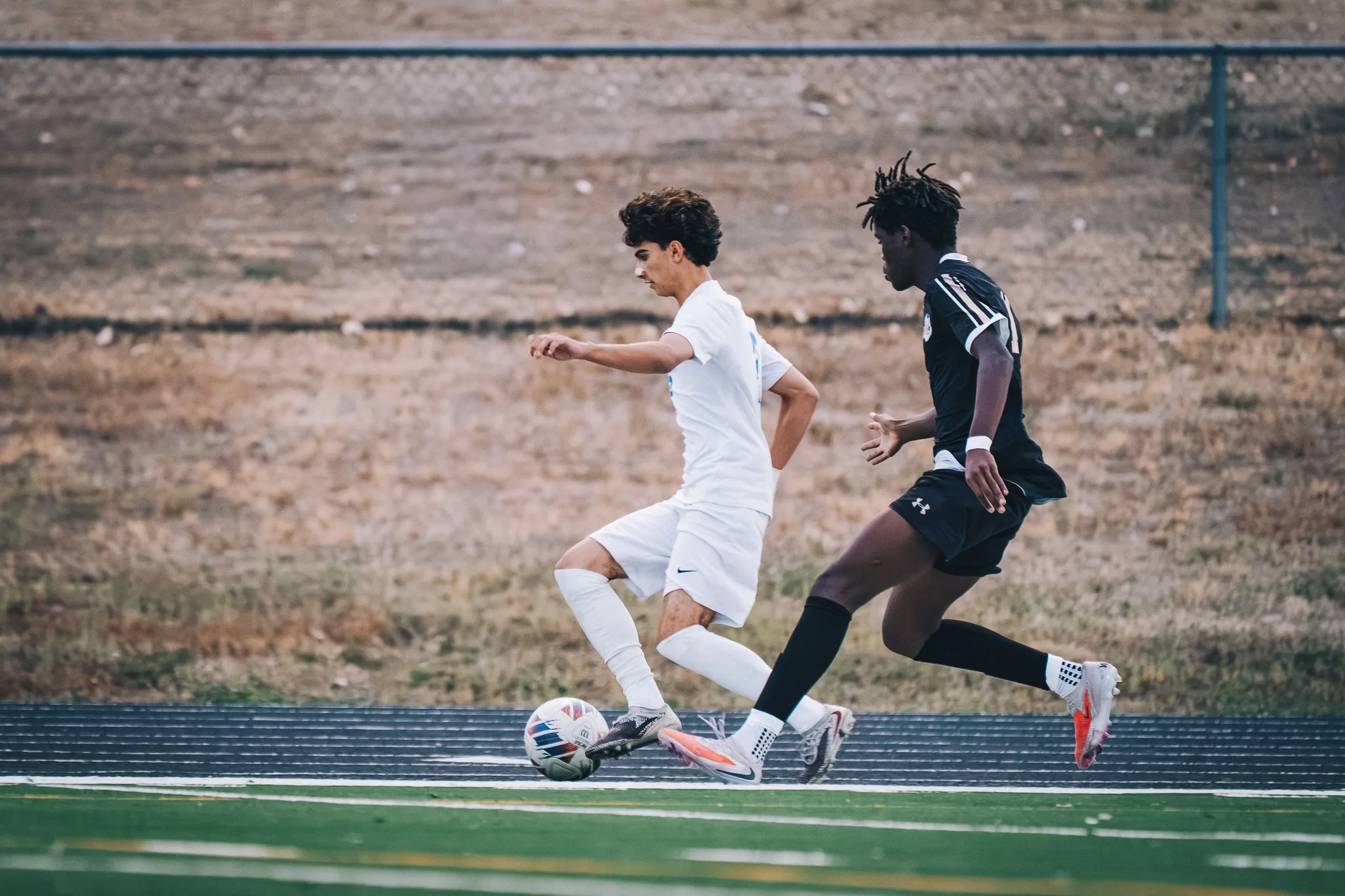 A Centaurus player in white and a Monarch player in black race for the ball along the edge of the field
