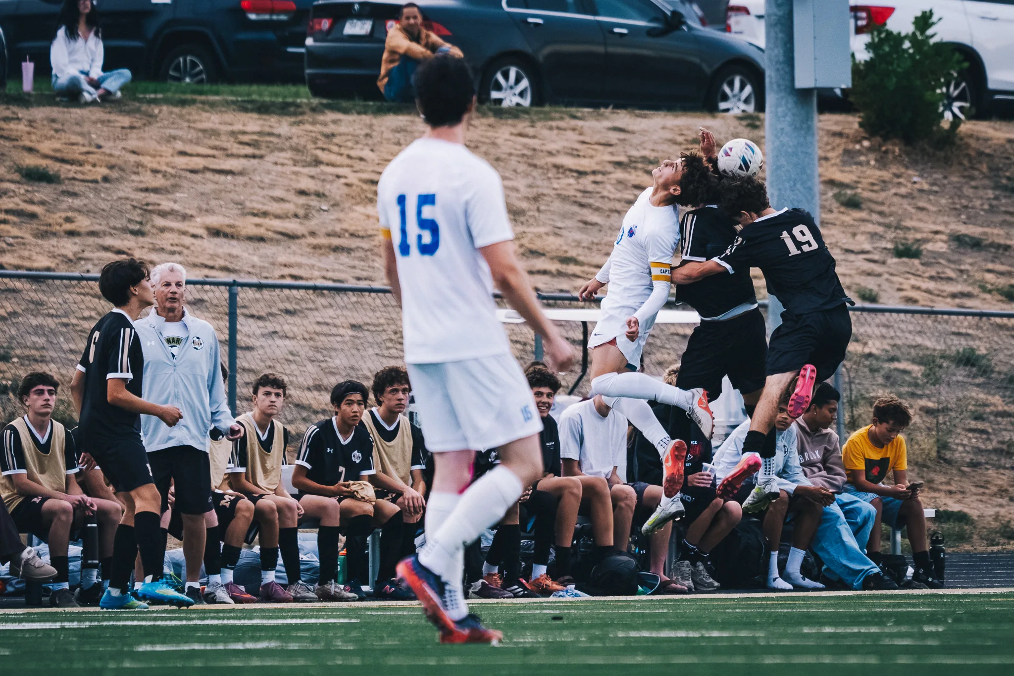 A Centaurus player and Monarch number 19 go up together for a header while Centaurus number 15 watches, the Monarch bench behind