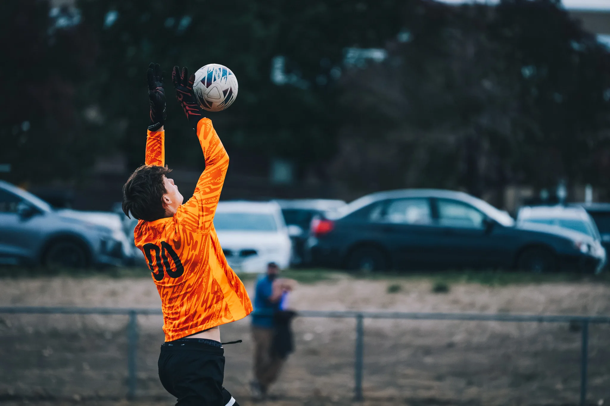 A goalkeeper in orange, number 00, reaches up to catch the ball