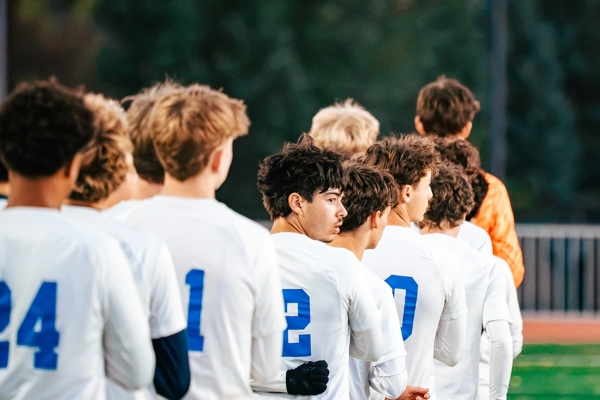 Before kickoff, Centaurus players stand shoulder to shoulder in a line, one turning his head to look down the row, the goalkeeper in orange near the end