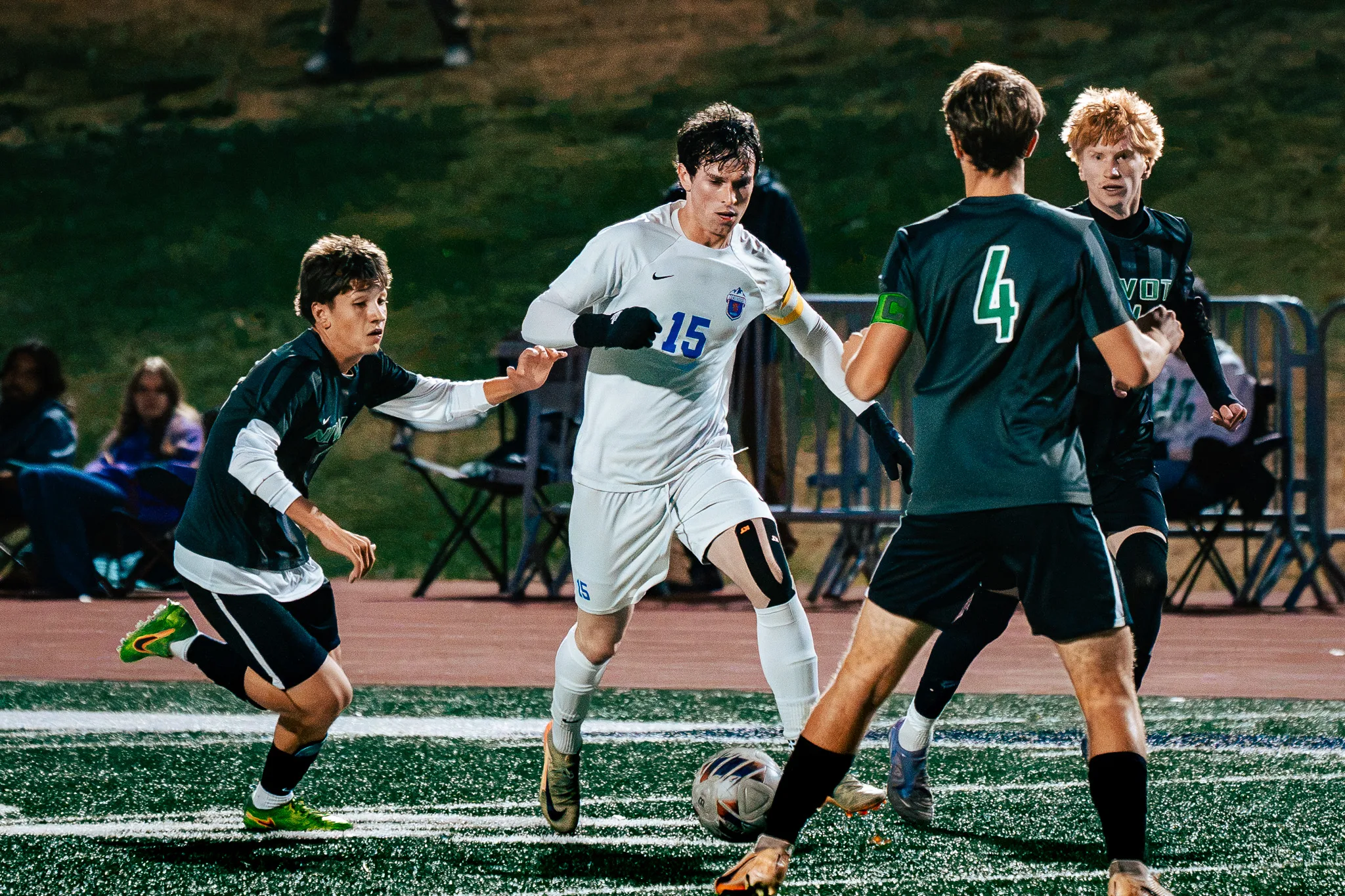 Centaurus number 15 dribbles at Niwot number 4 as two more Niwot players close in, one with red hair, spectators in lawn chairs behind