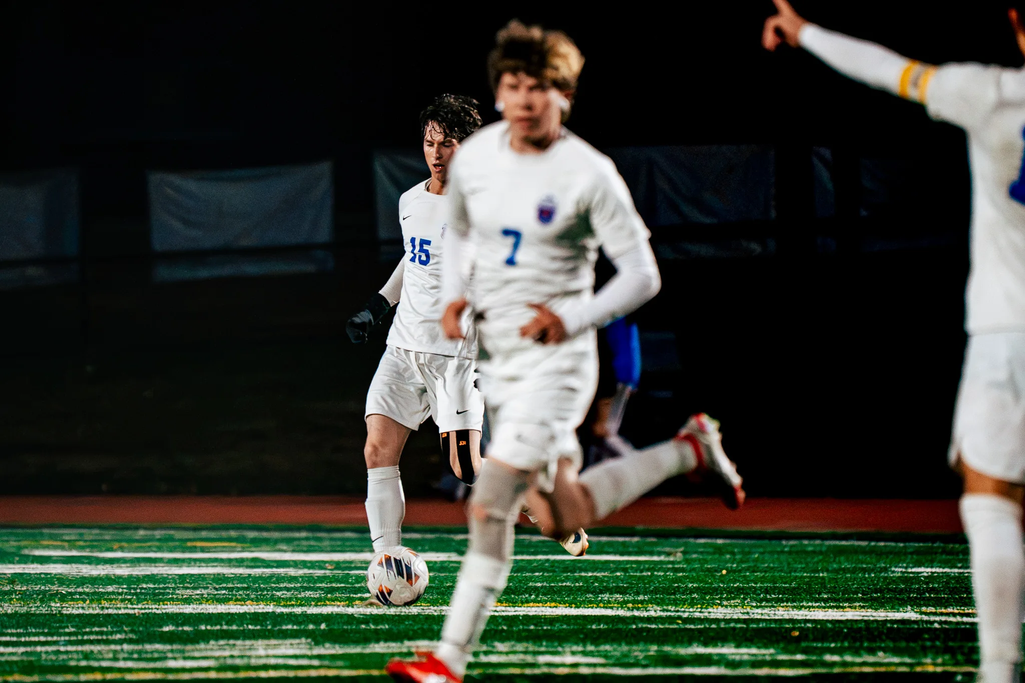 At night, Centaurus number 15 brings the ball forward as teammate number 7 runs past in a blur and a teammate in a yellow armband points from the right edge