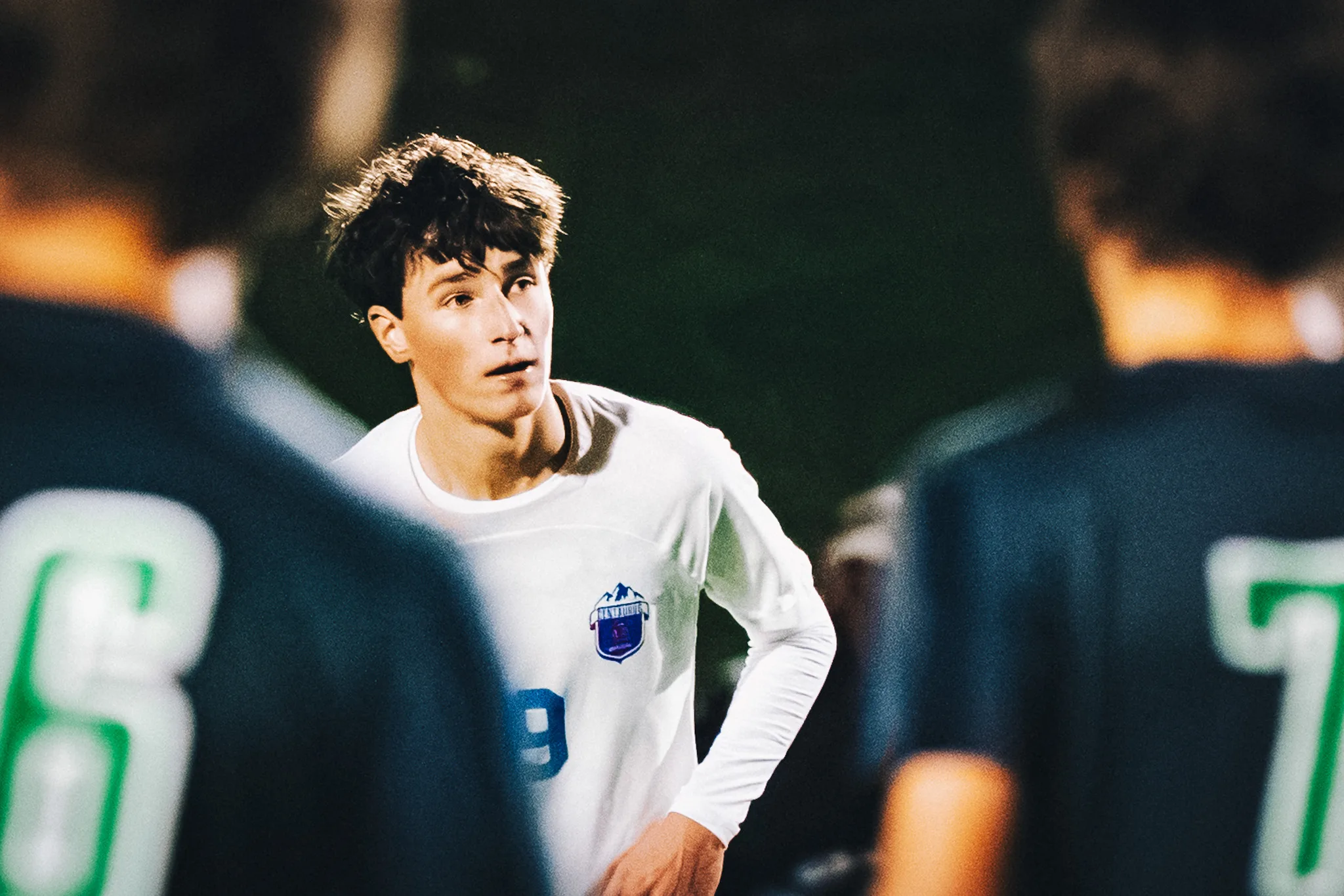 Hand on his hip, Centaurus number 9 looks up the field between two blurred Niwot players at night