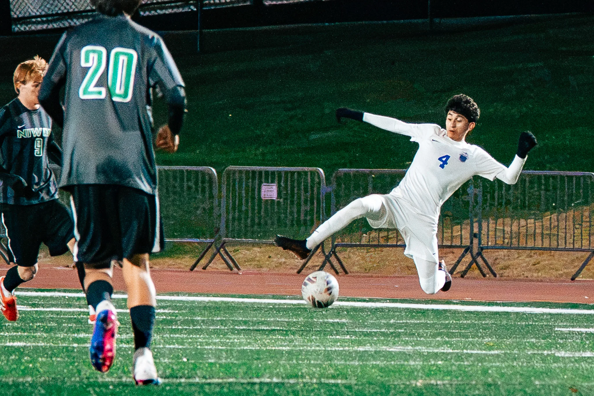 Centaurus number 4 leans back and stretches a leg out to block the ball as Niwot number 20 runs at him and another Niwot player follows
