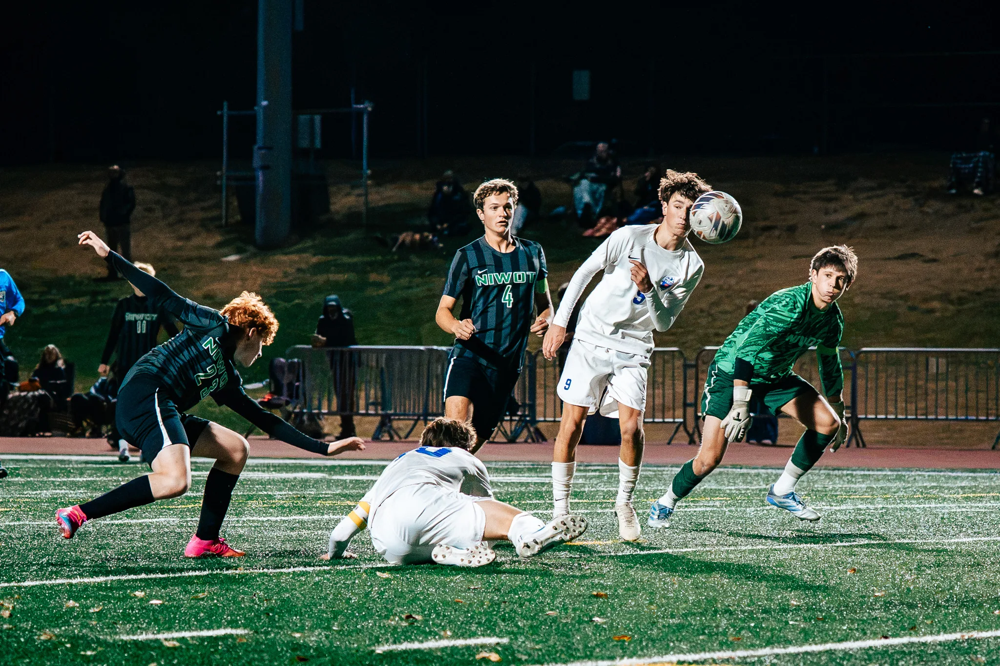Centaurus number 9 heads the ball in front of the Niwot goalkeeper in green as Niwot number 4 watches, a Niwot player with red hair lunges in and a Centaurus player lies on the turf