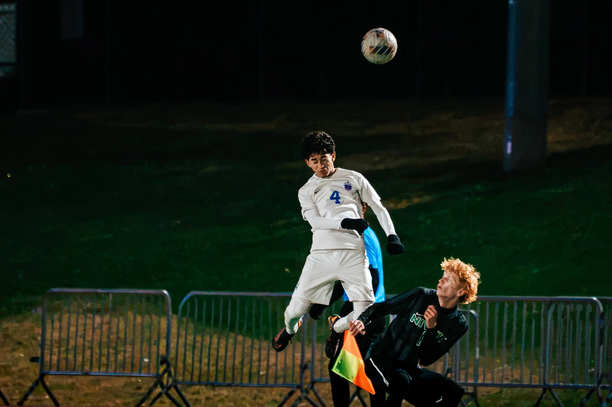 Centaurus number 4 leaps for a high ball above a Niwot player with red hair, an assistant referee's flag at the bottom of the frame