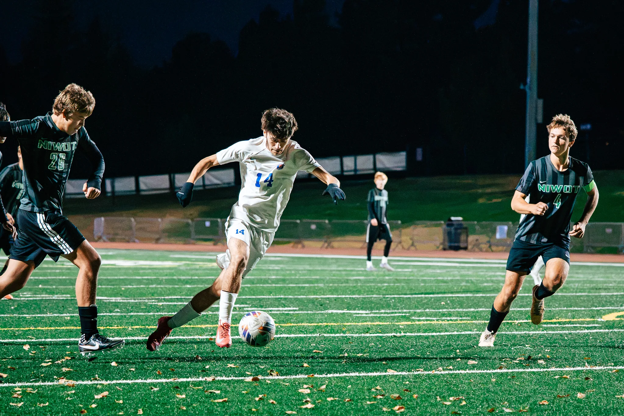 Centaurus number 14 drives the ball forward between Niwot numbers 26 and 4, fallen leaves scattered on the turf