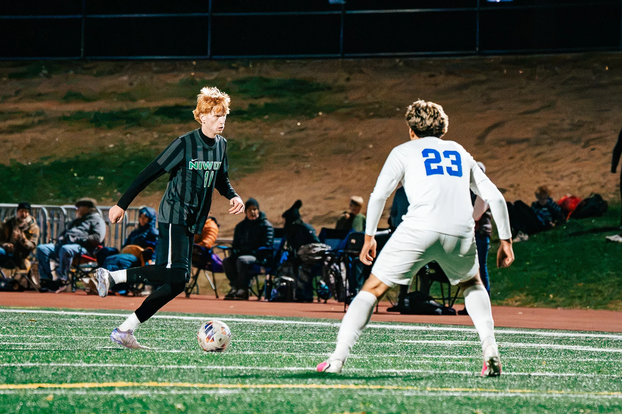 Niwot number 11, with red hair, dribbles at Centaurus number 23 in front of spectators in lawn chairs