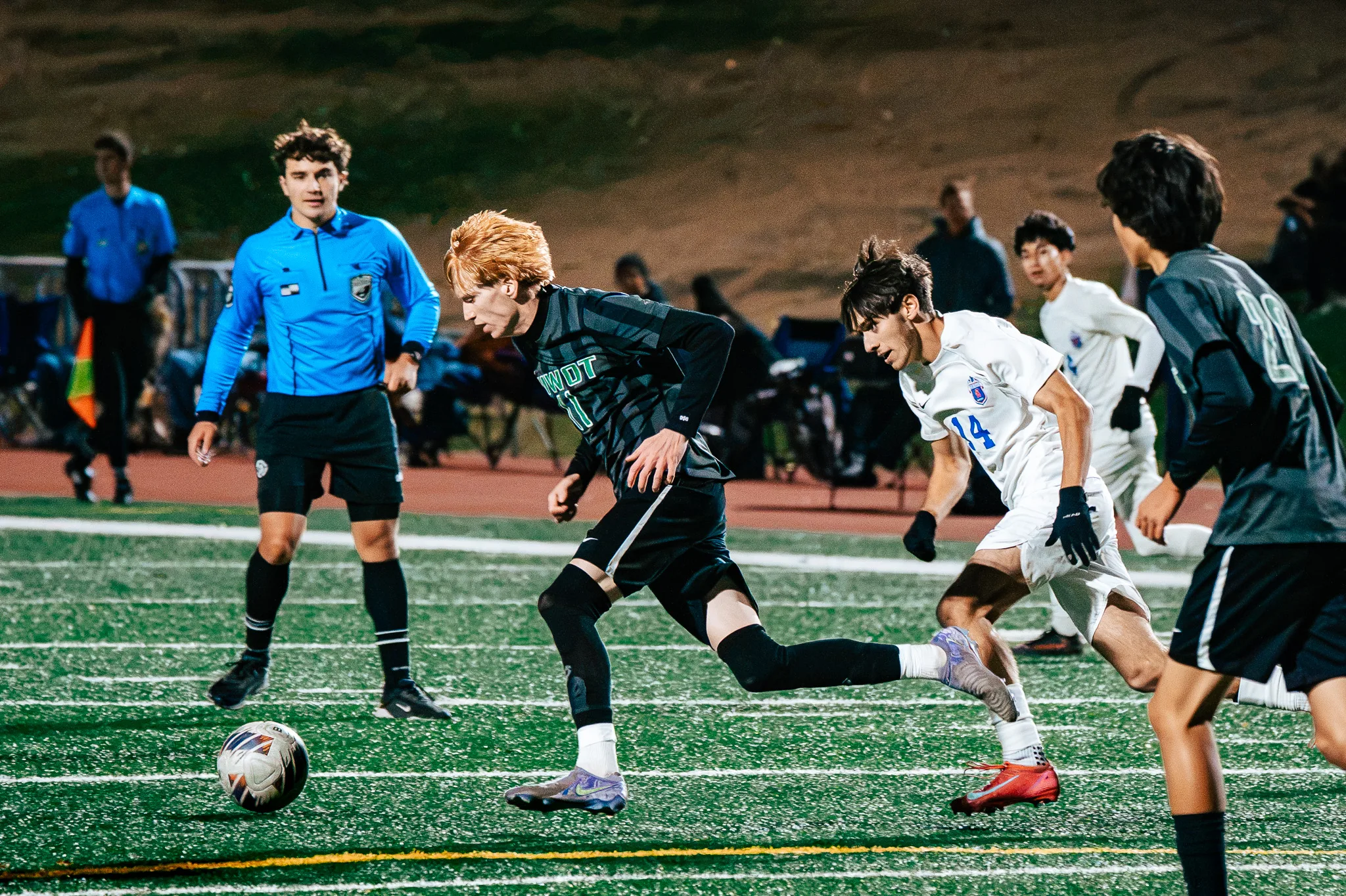 Niwot number 11 pushes the ball ahead as Centaurus number 14 chases him, a referee in blue watching from the left