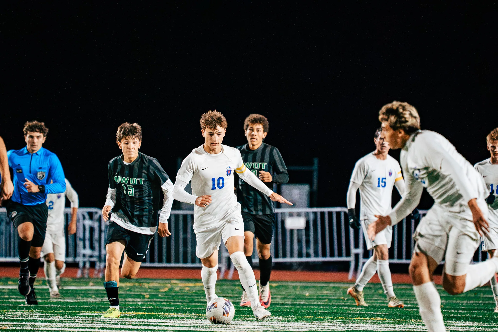 Centaurus number 10 in a captain's armband dribbles up the field as Niwot number 15 and another Niwot player chase, a referee in blue following