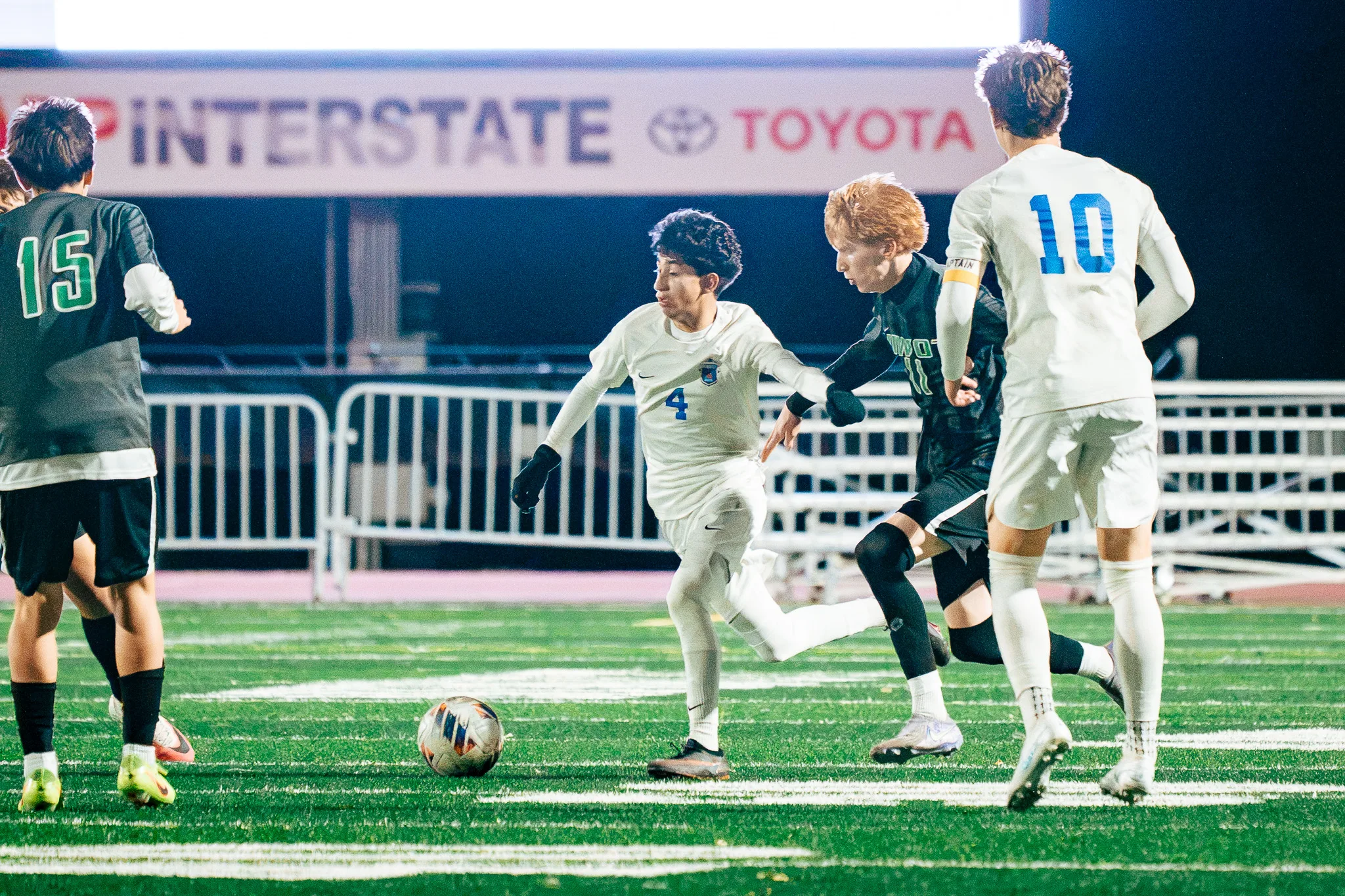 Centaurus number 4 cuts the ball away from Niwot number 11 as Niwot number 15 and Centaurus number 10 close in, a sponsor banner above them