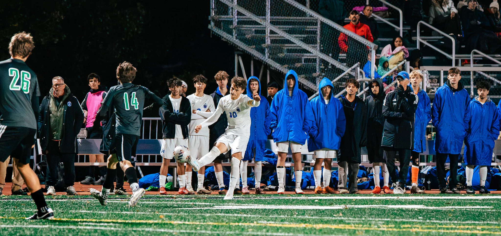 Centaurus number 10 kicks the ball in front of his bench, teammates in blue parkas watching from the sideline as Niwot numbers 26 and 14 close in