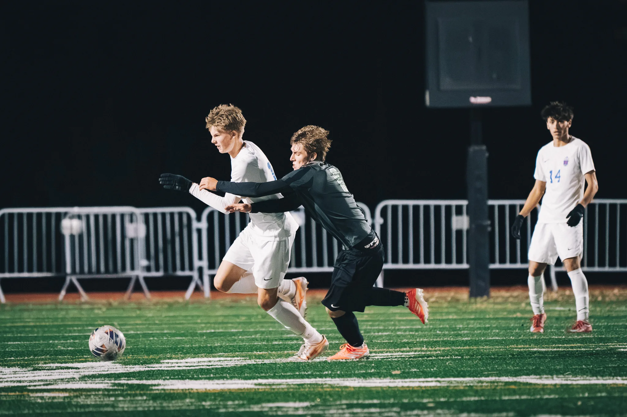 A Niwot player wraps an arm across a Centaurus player as they chase the ball, Centaurus number 14 watching from the right
