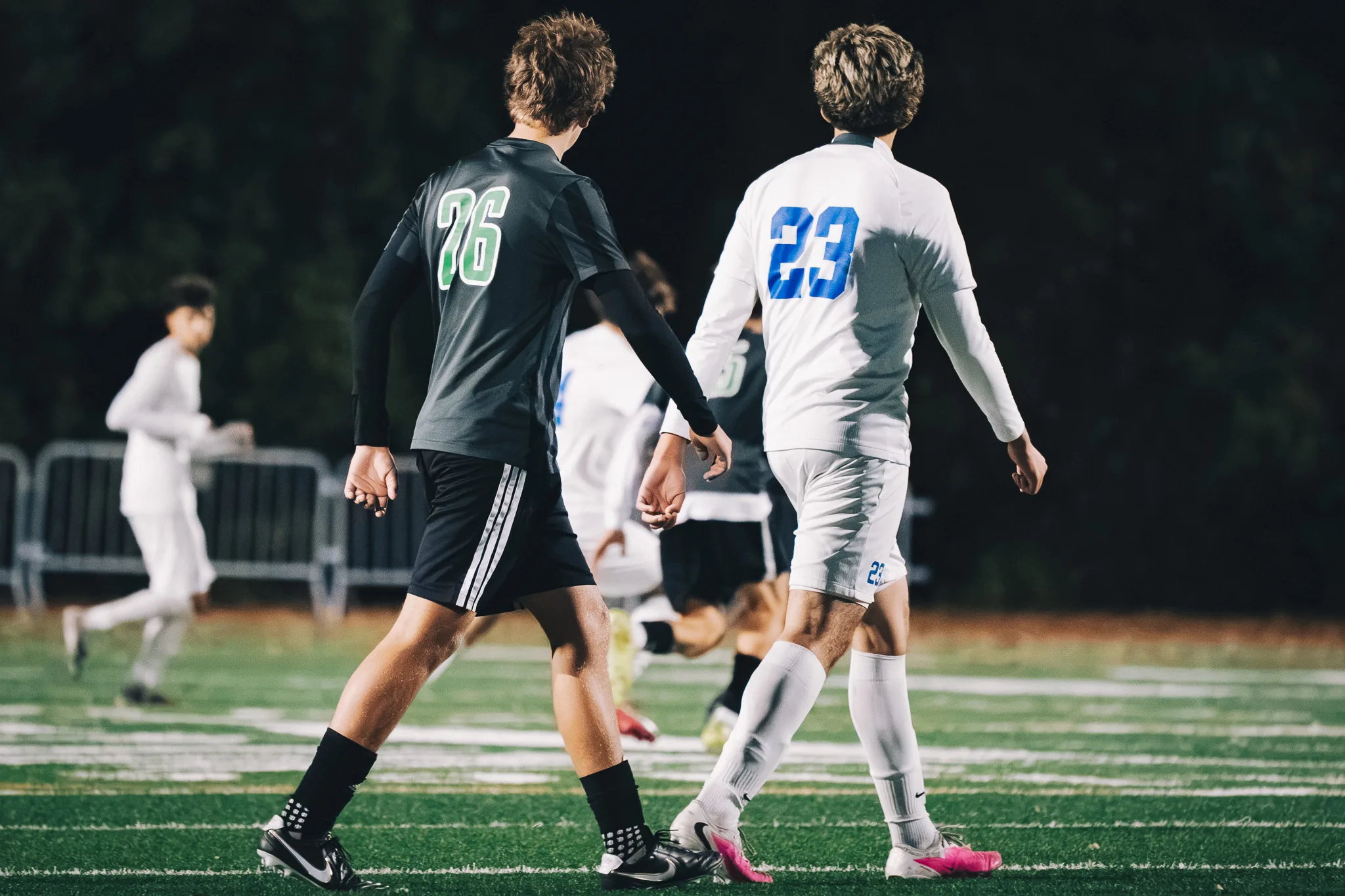 Seen from behind, Niwot number 76 and Centaurus number 23 walk side by side up the field, more players ahead of them