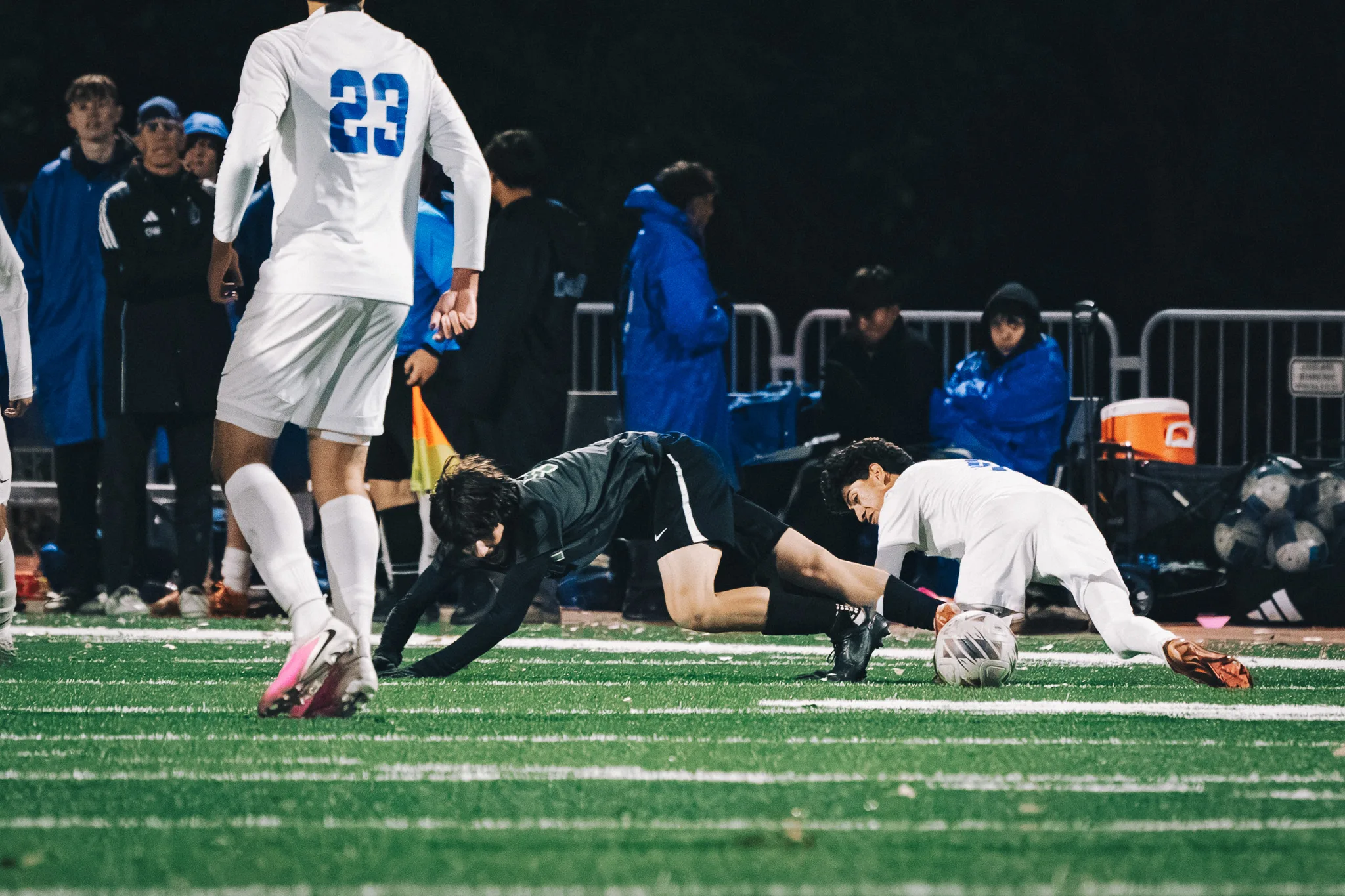 A Niwot player and a Centaurus player sprawl on the turf beside the ball as Centaurus number 23 looks on, the Centaurus bench behind